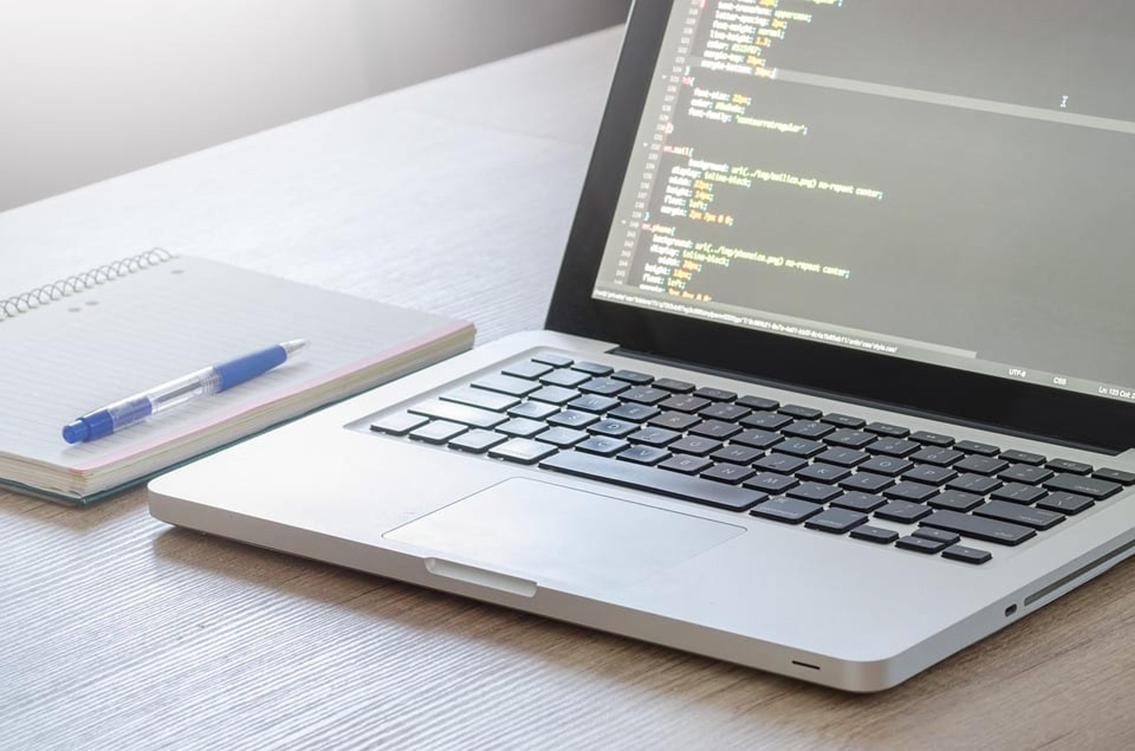 laptop open on a table next to a notebook and pen.