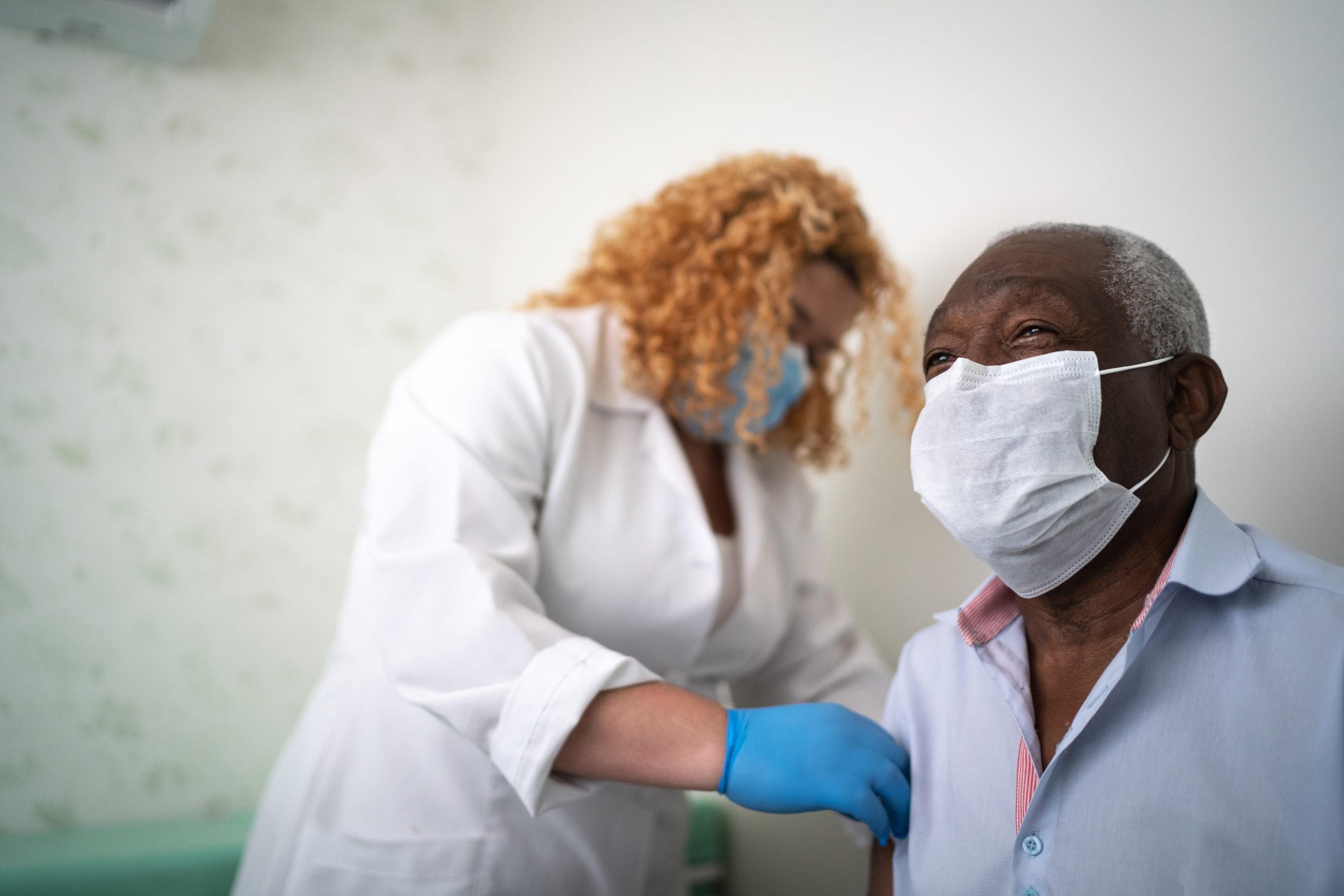 A Black man in a mask smiles as he prepares to receive a vaccine.
