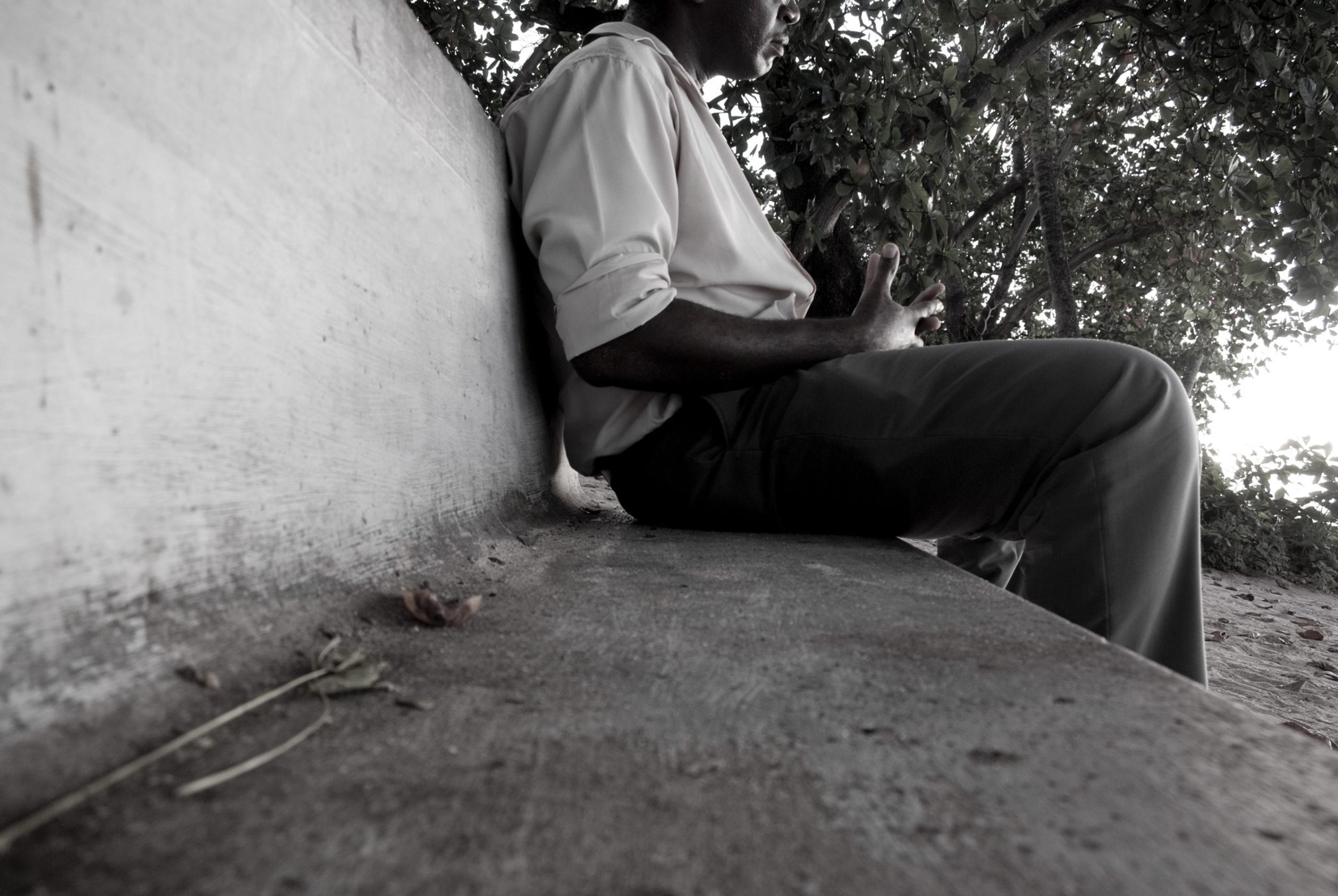 Black and white image of man sitting on a bench.