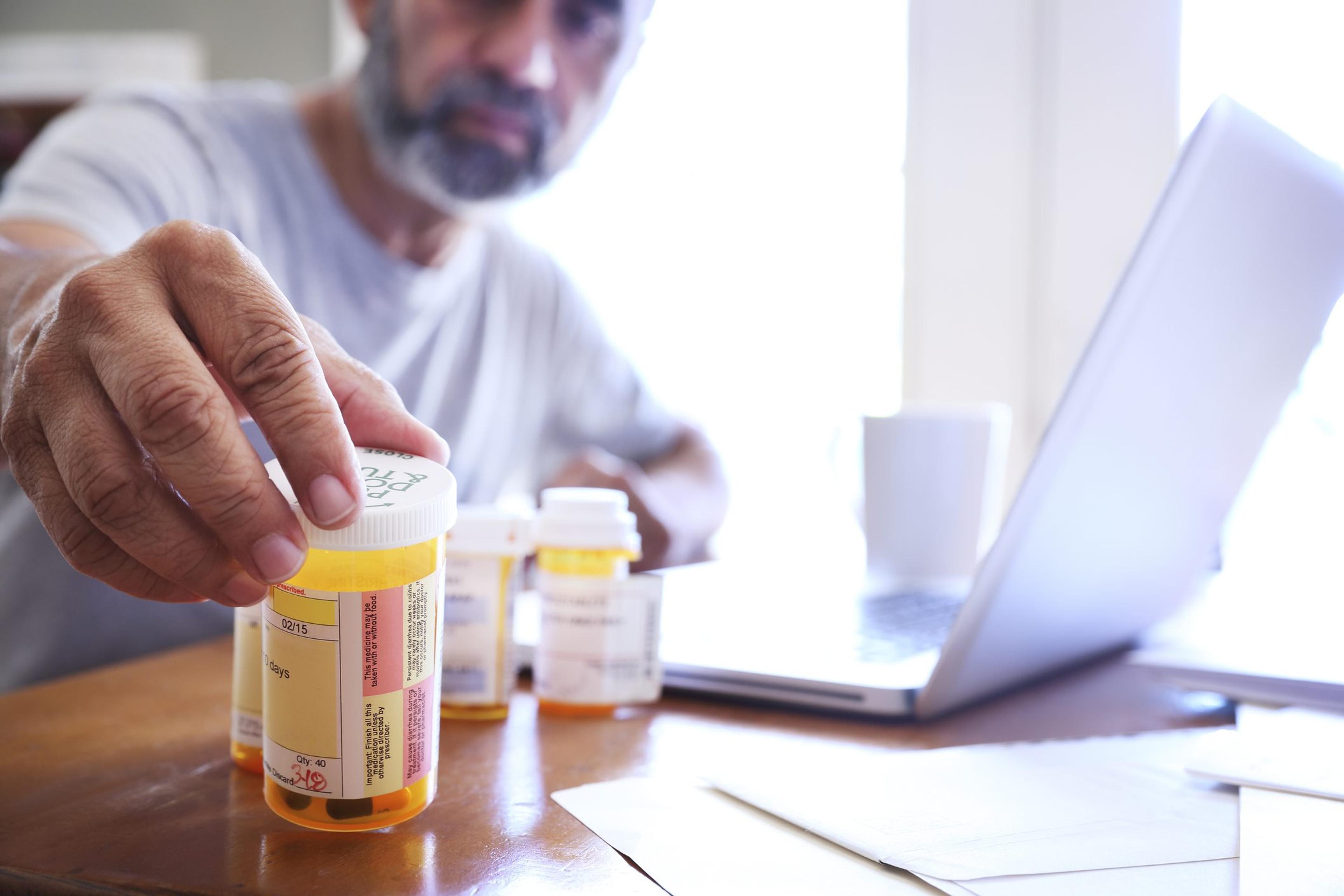 Man reaches for his prescription bottles at the table