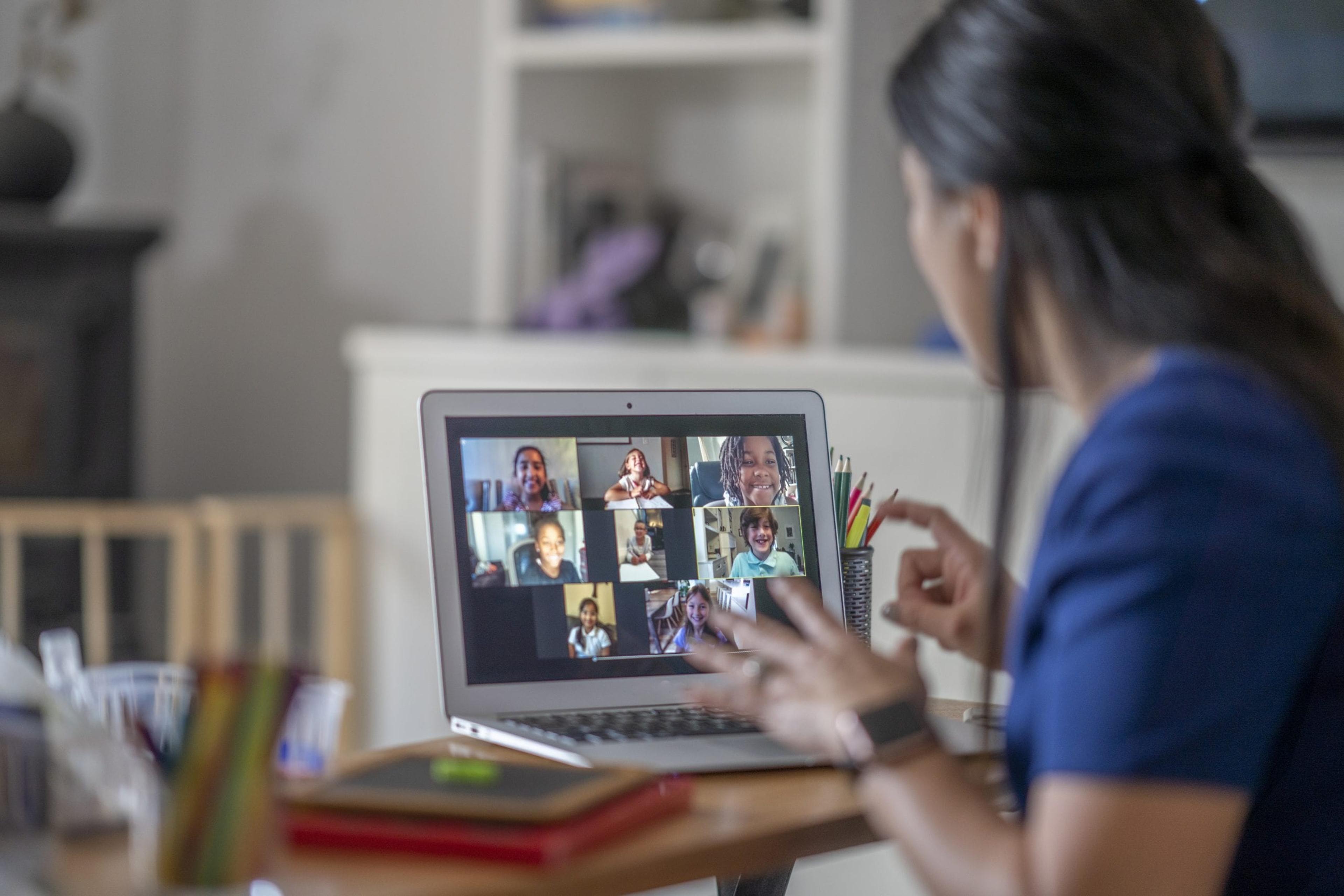Teacher instructs young students in front of a computer screen for virtual learning.