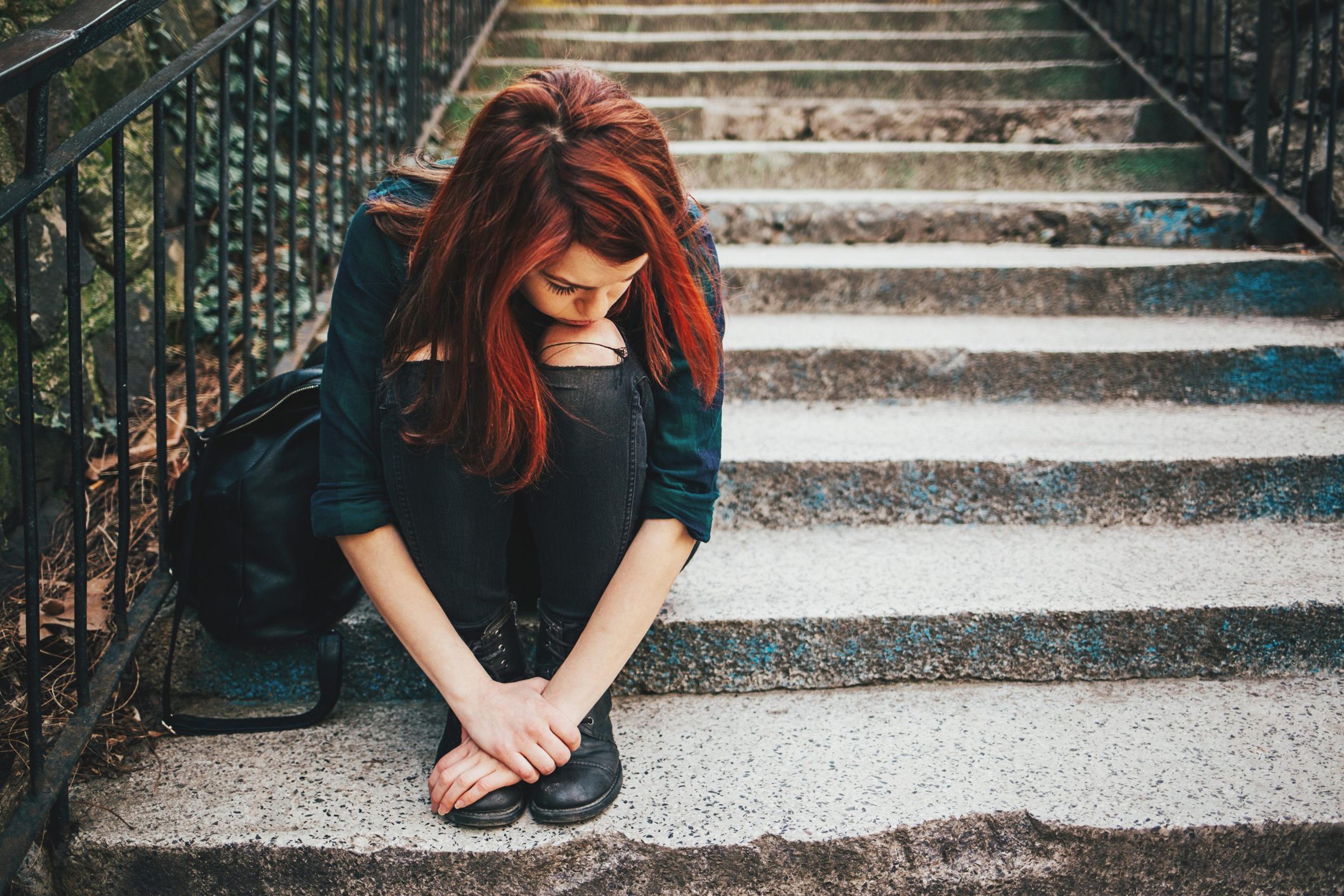 Sad female teenager sitting on the stairs struggling with mental health