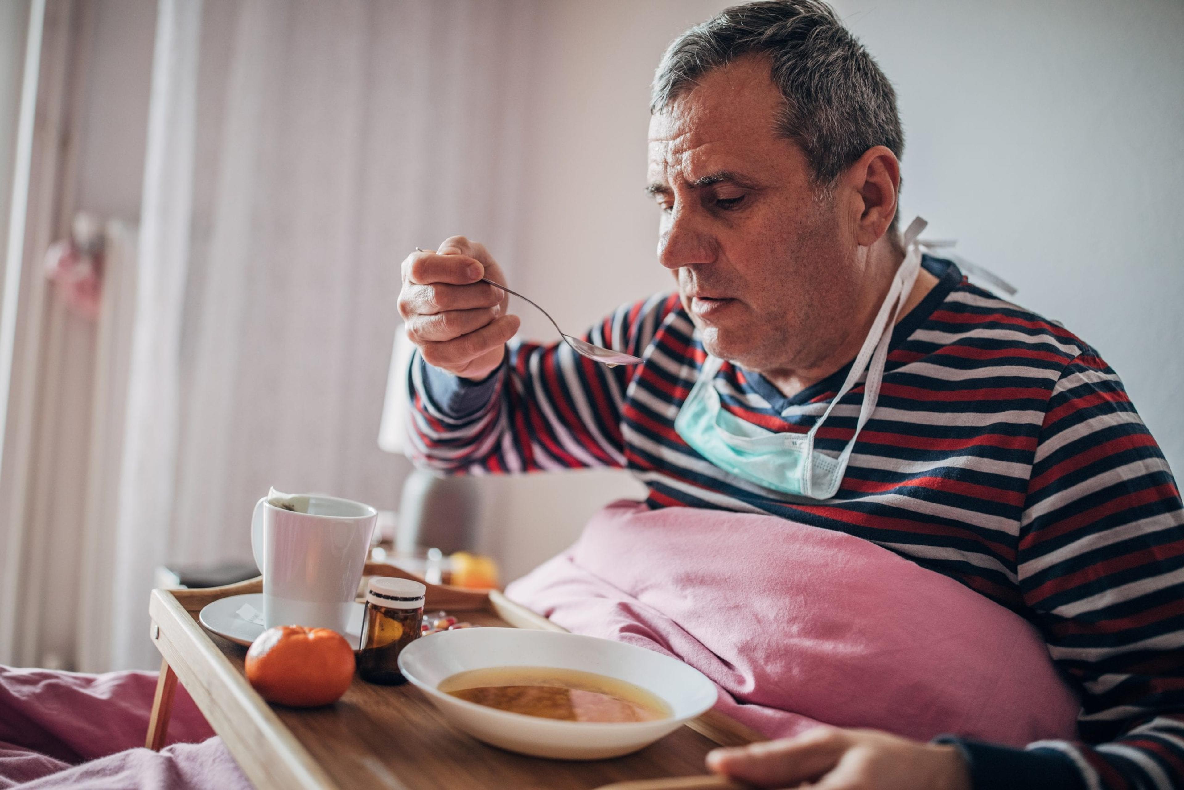 Sick man wearing a mask eats in bed