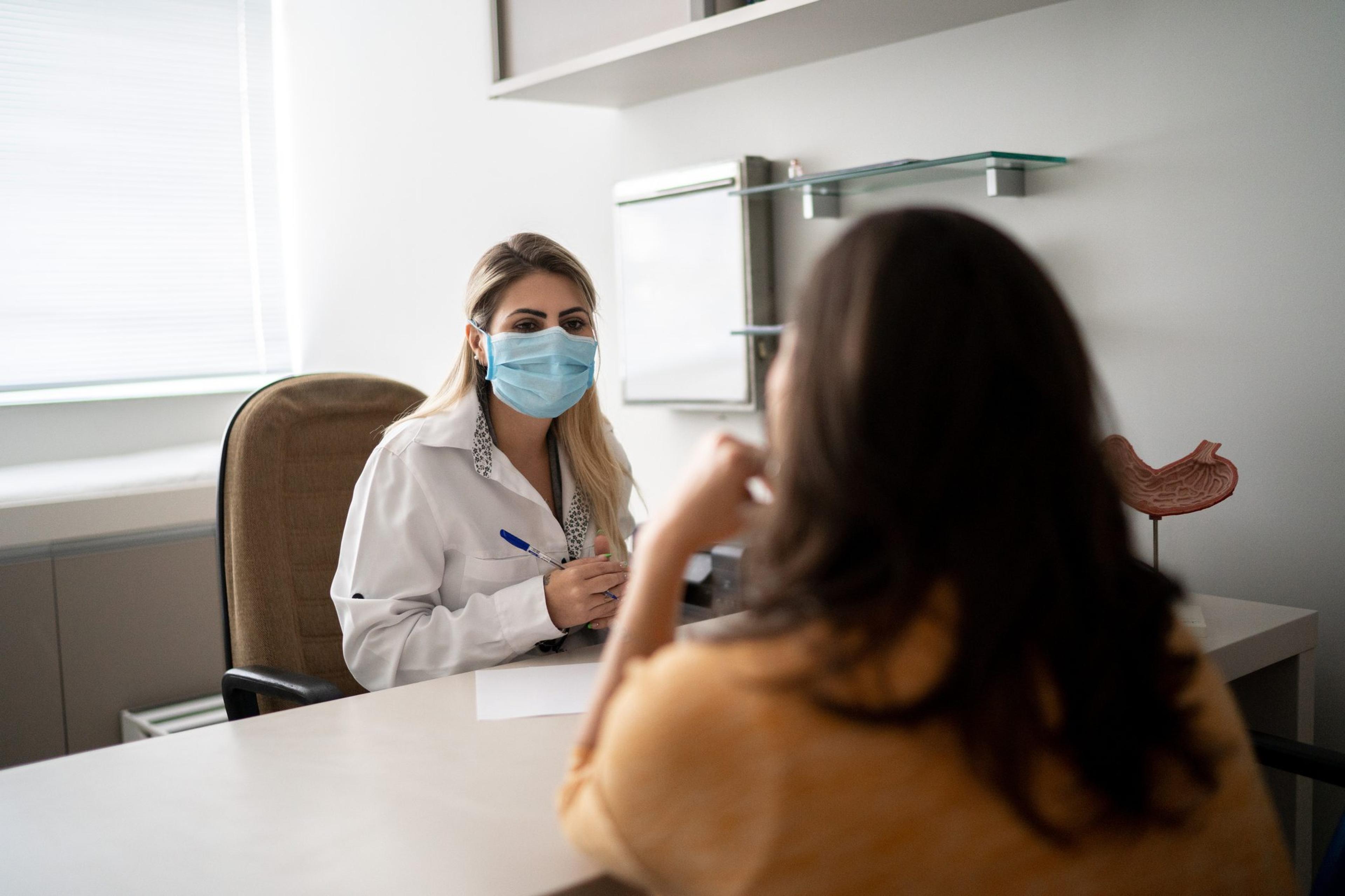 Female doctor wearing a mask speaking with female millennial patient