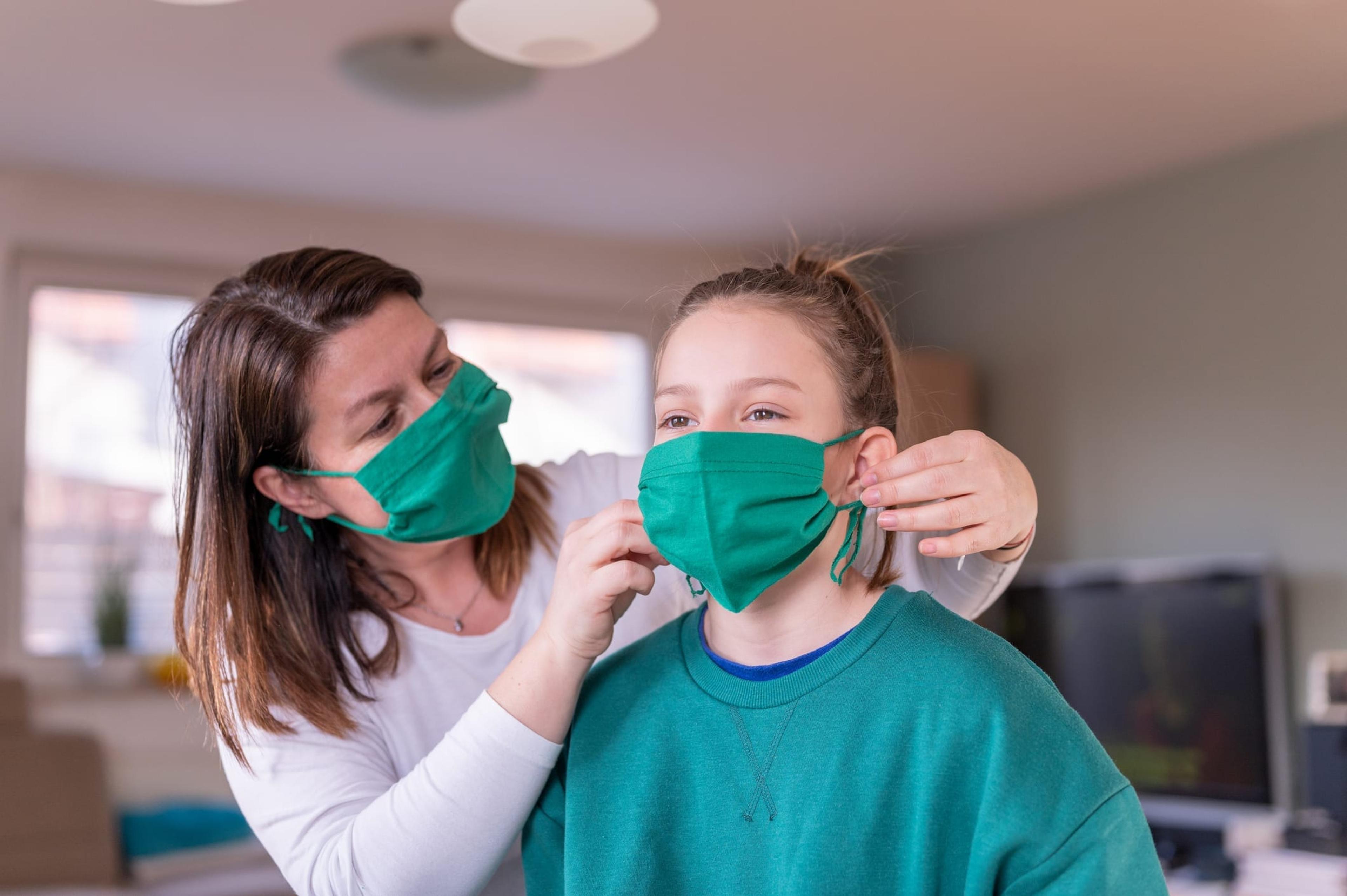 Mother wearing a homemade protective mask and putting one to her daughter