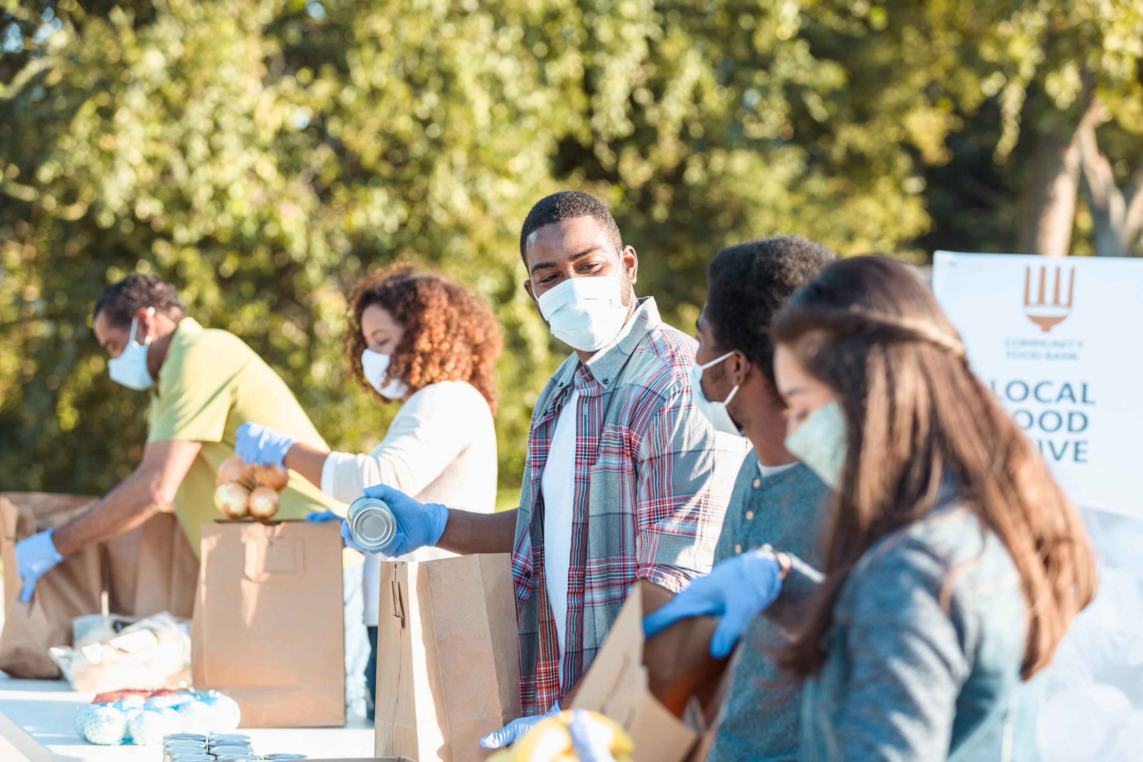 Group of masked individuals pack brown bags of food in an organized line.