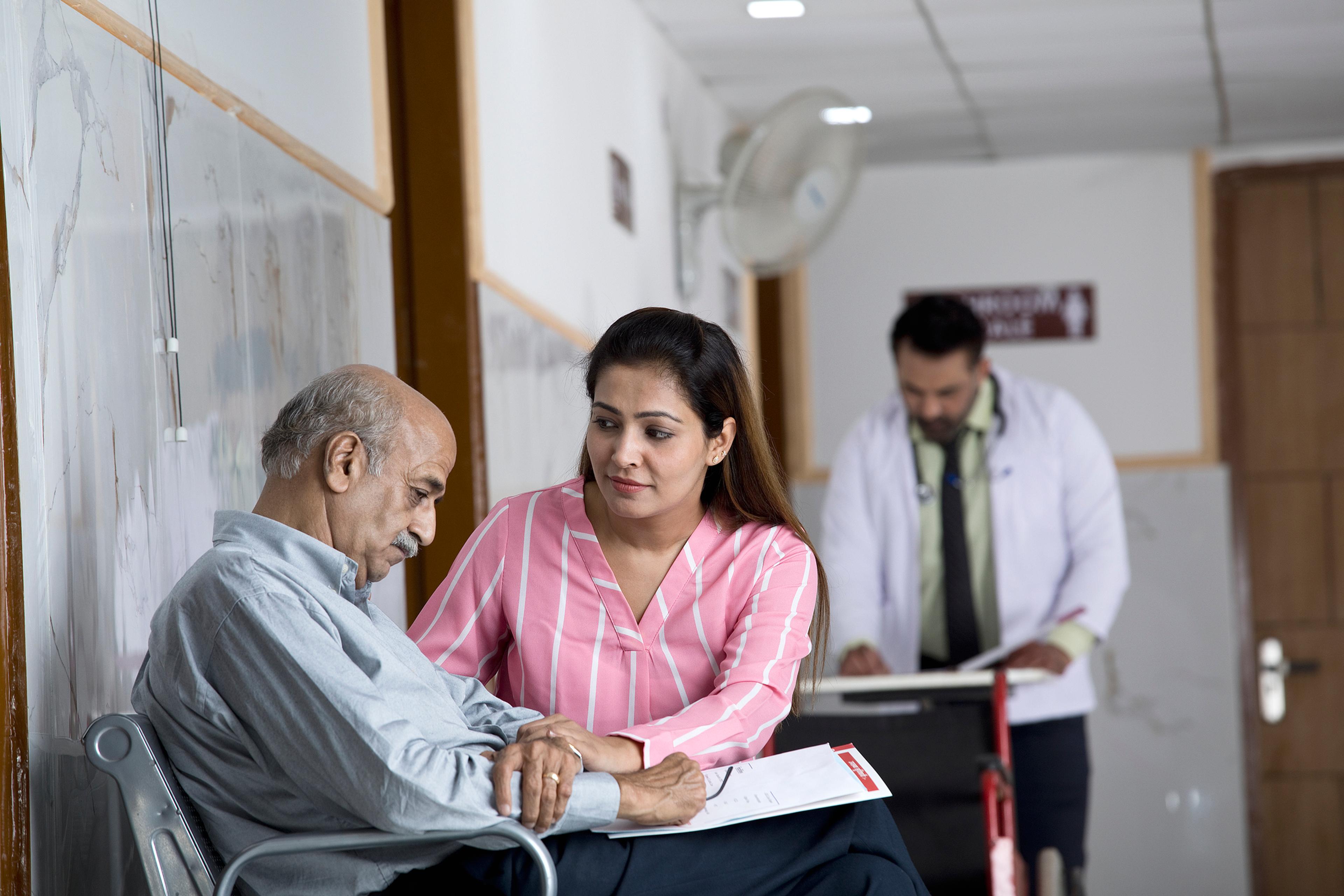 An adult woman consoles her father in a doctor's office.