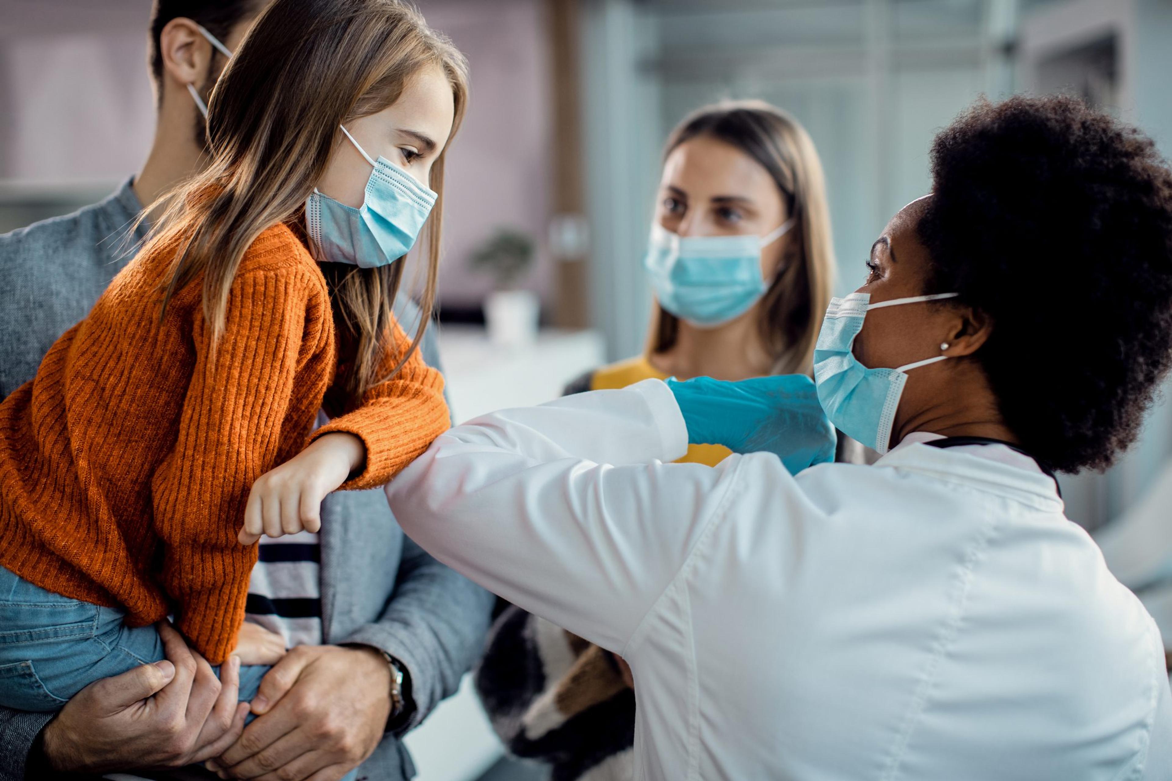 Little girl wearing a mask bumps elbows with pediatrician wearing a mask