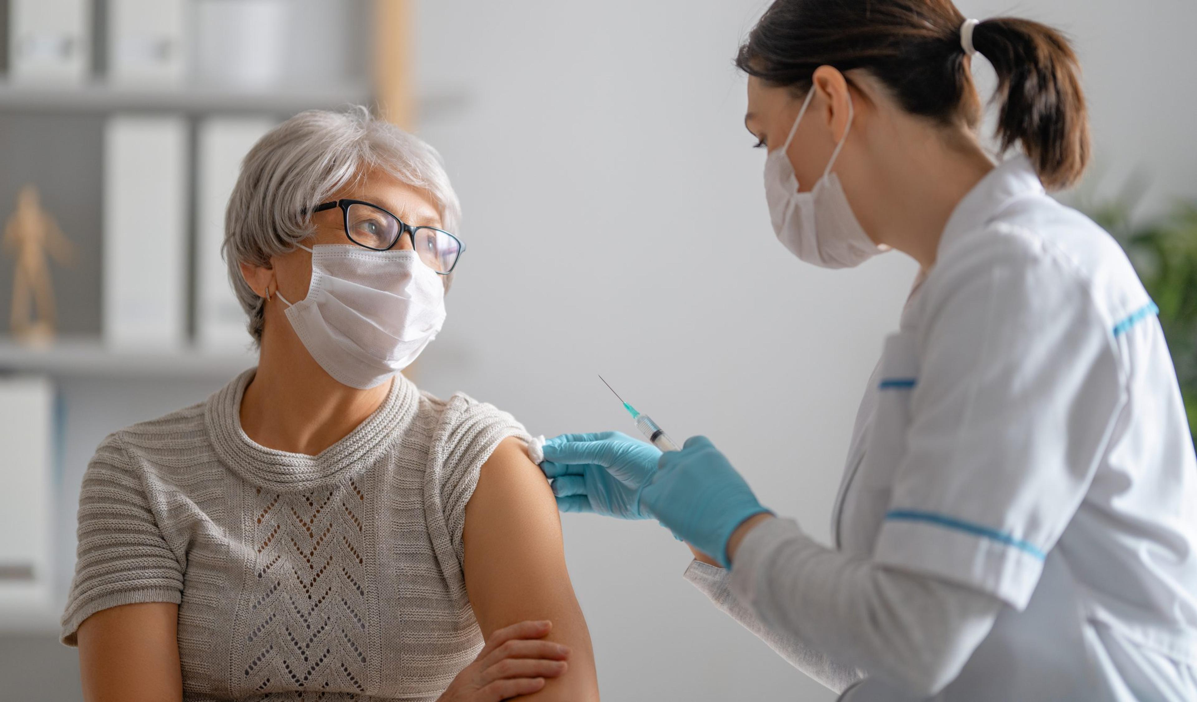 Doctor wearing a mask and gloves gives an older woman a COVID booster vaccine