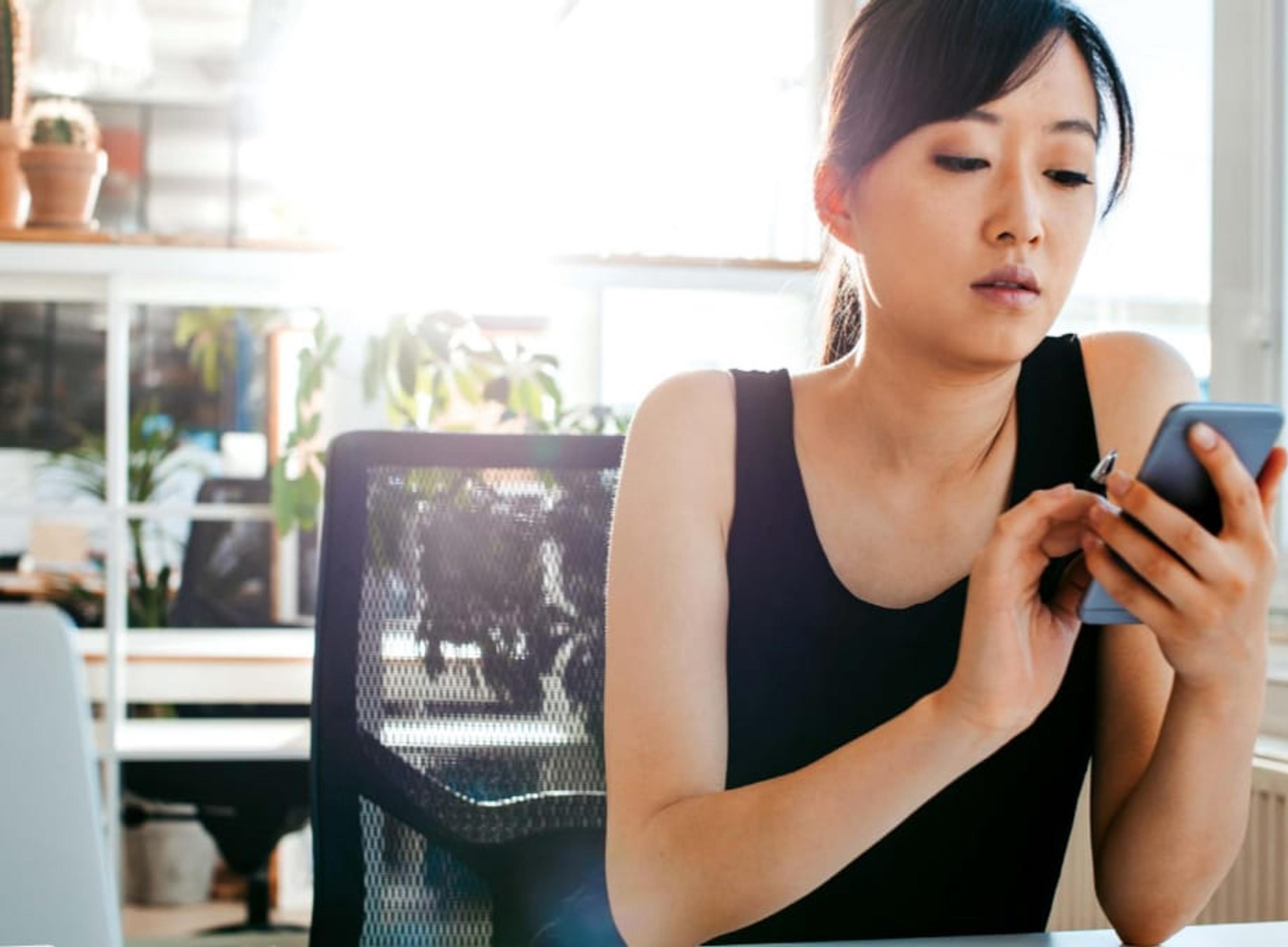 A woman working at a desk reads her smartphone