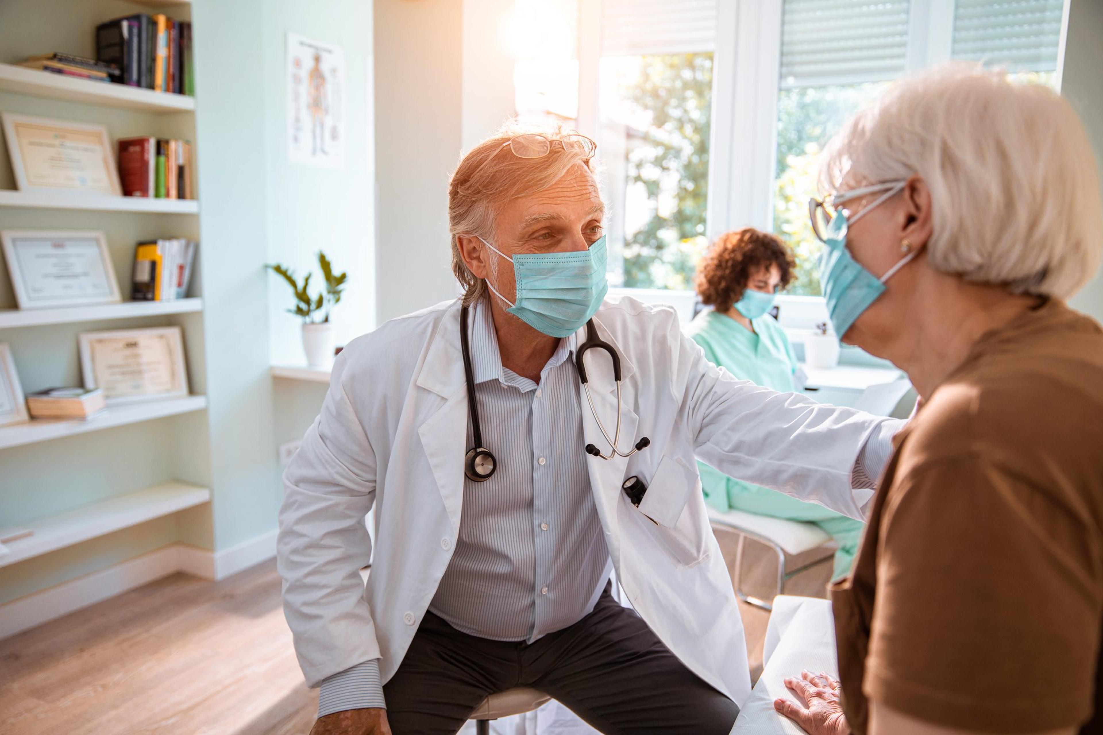 Masked doctor comforts a masked older female patient