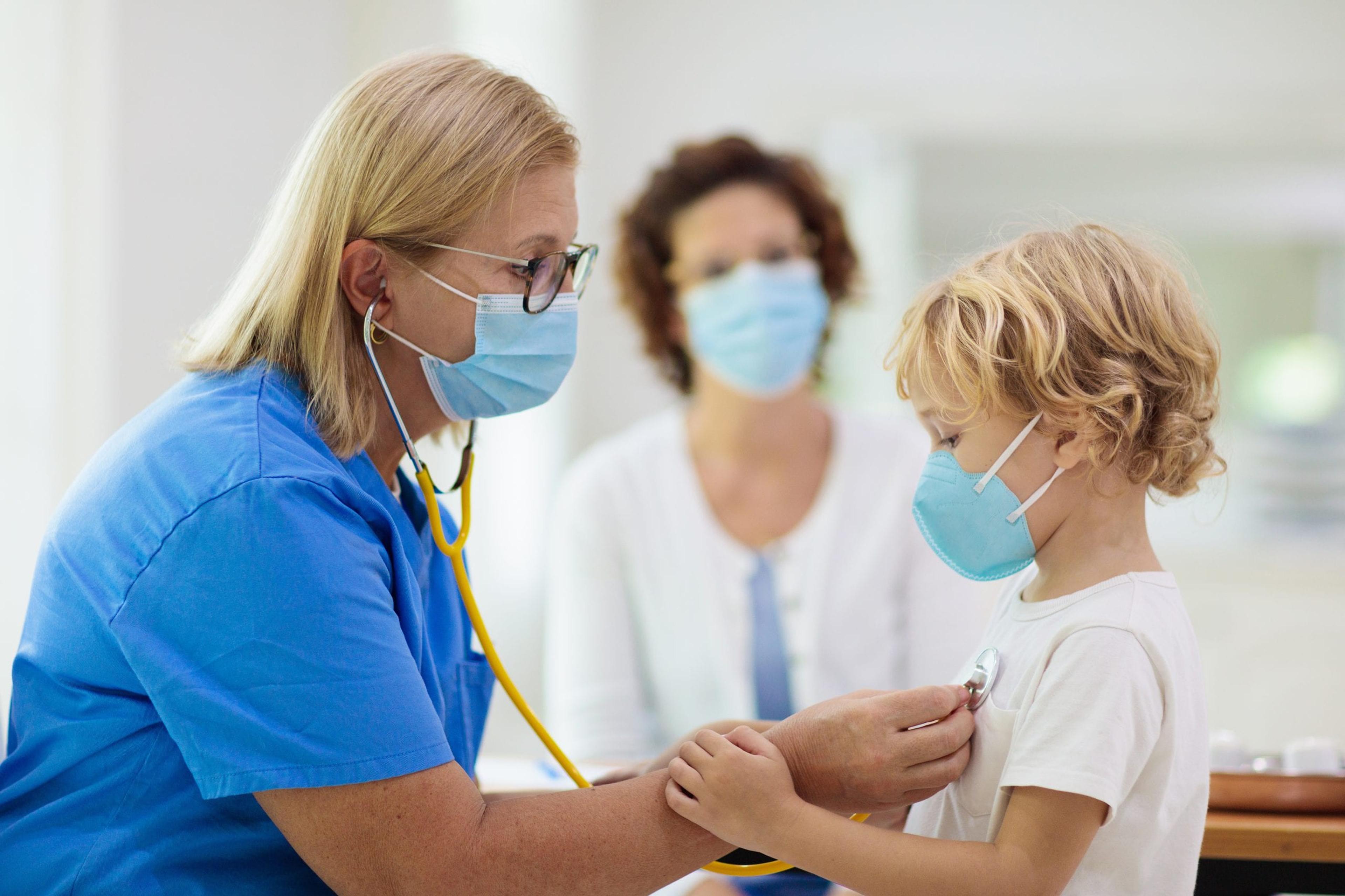 Doctor examining a small child. Both are wearing masks.