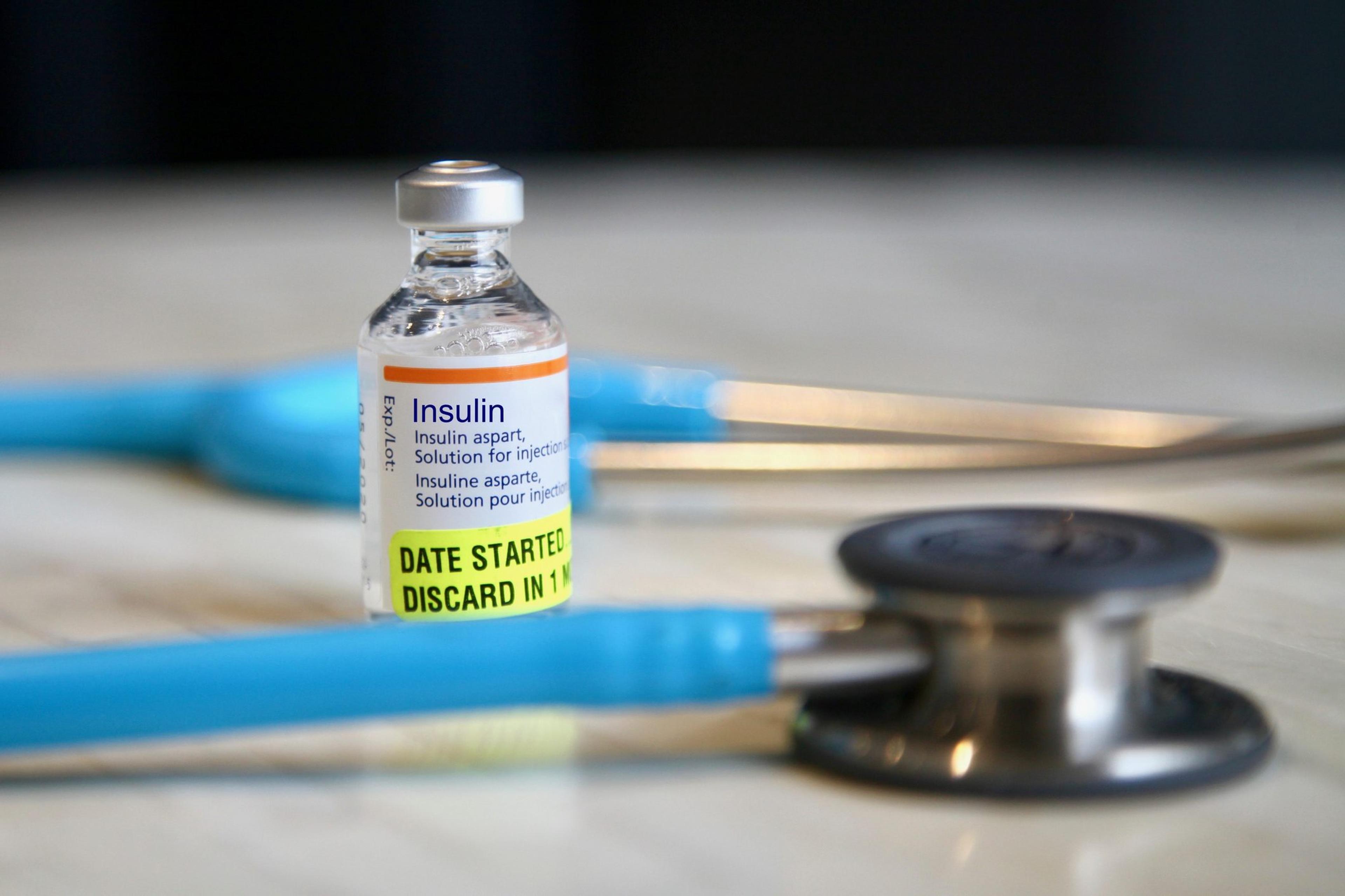 Lower-cost insulin vial sitting on a table next to a stethoscope