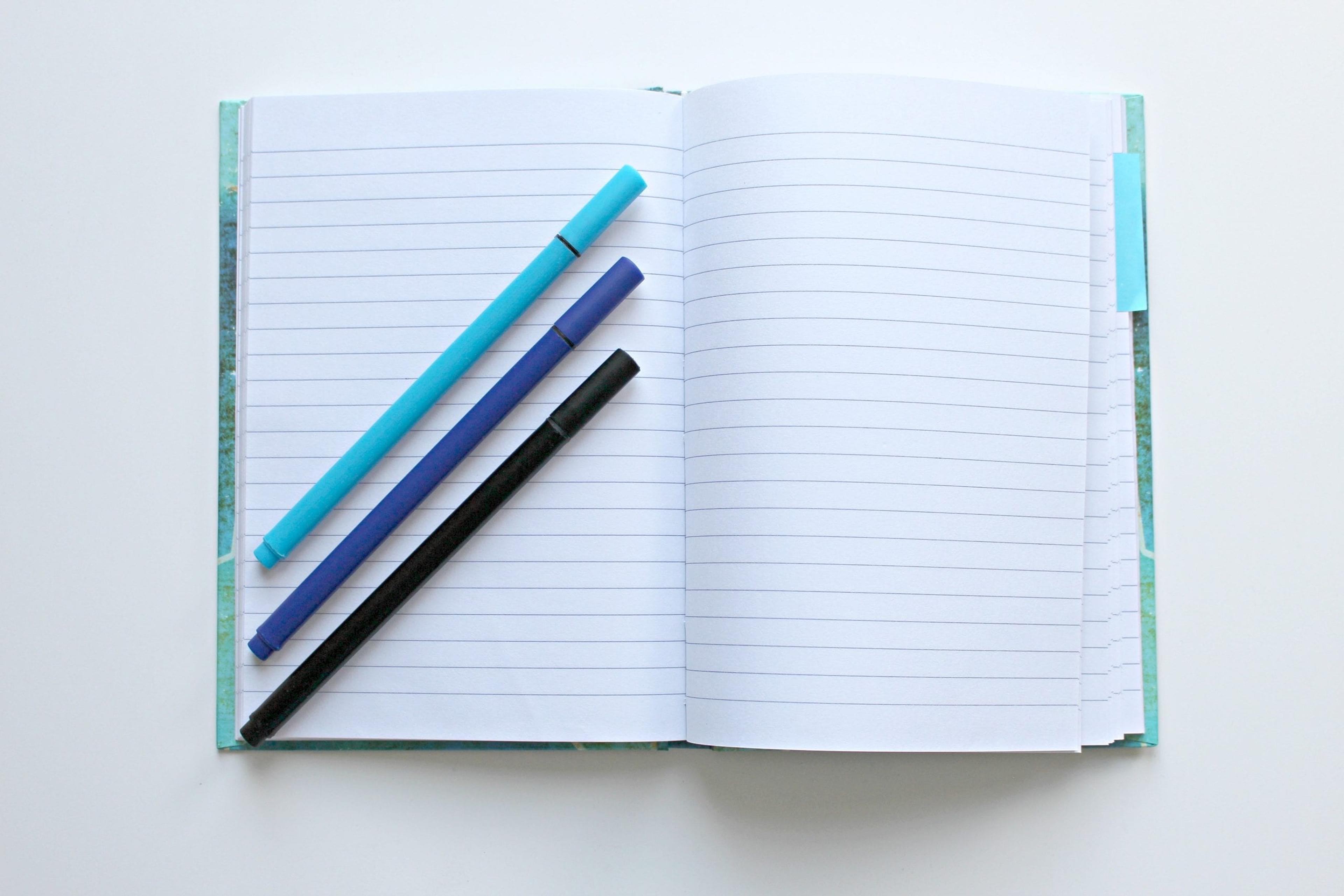 A notebook lays open with pens on the page