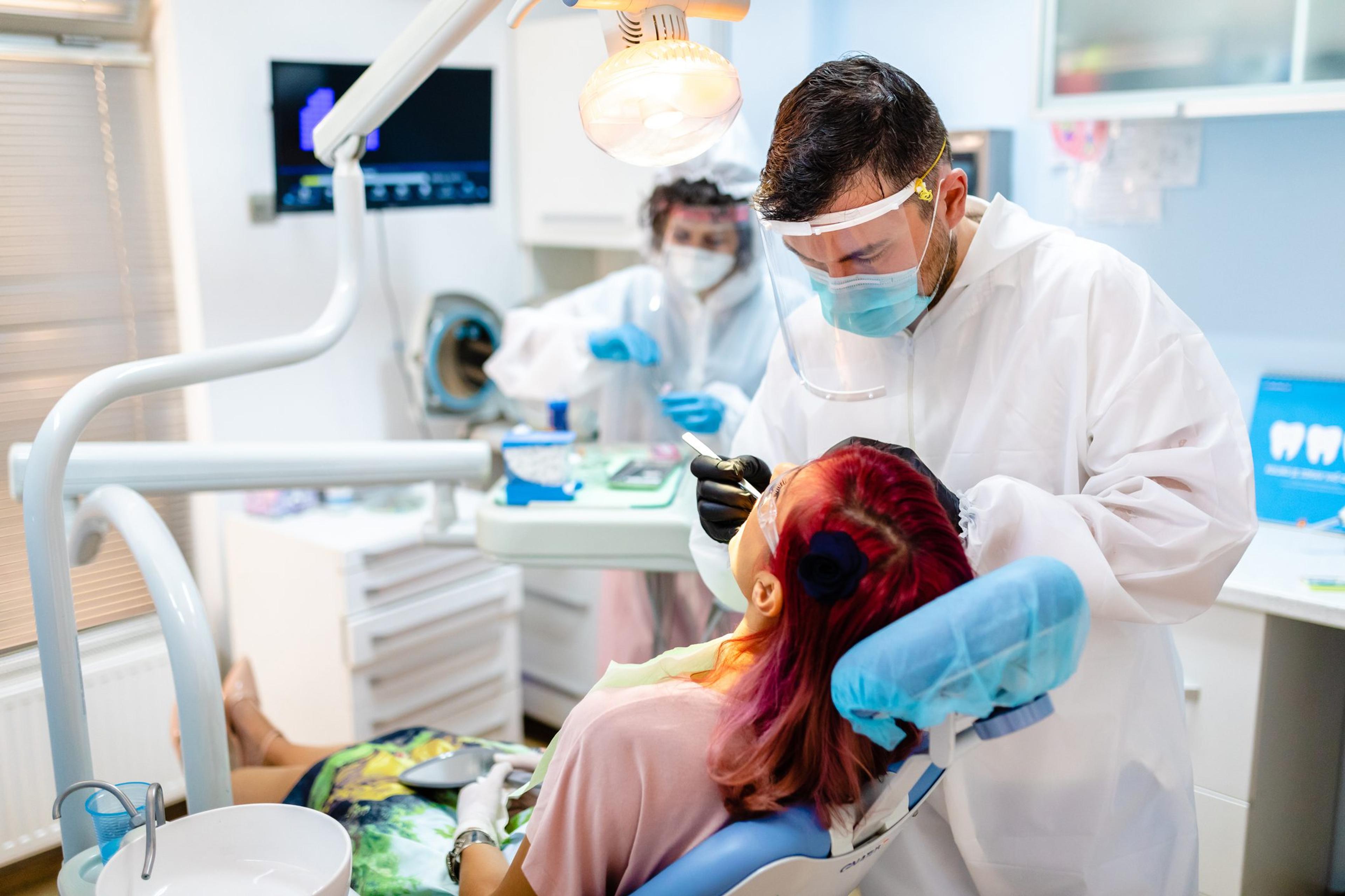 Dentist wearing PPE helps female patient