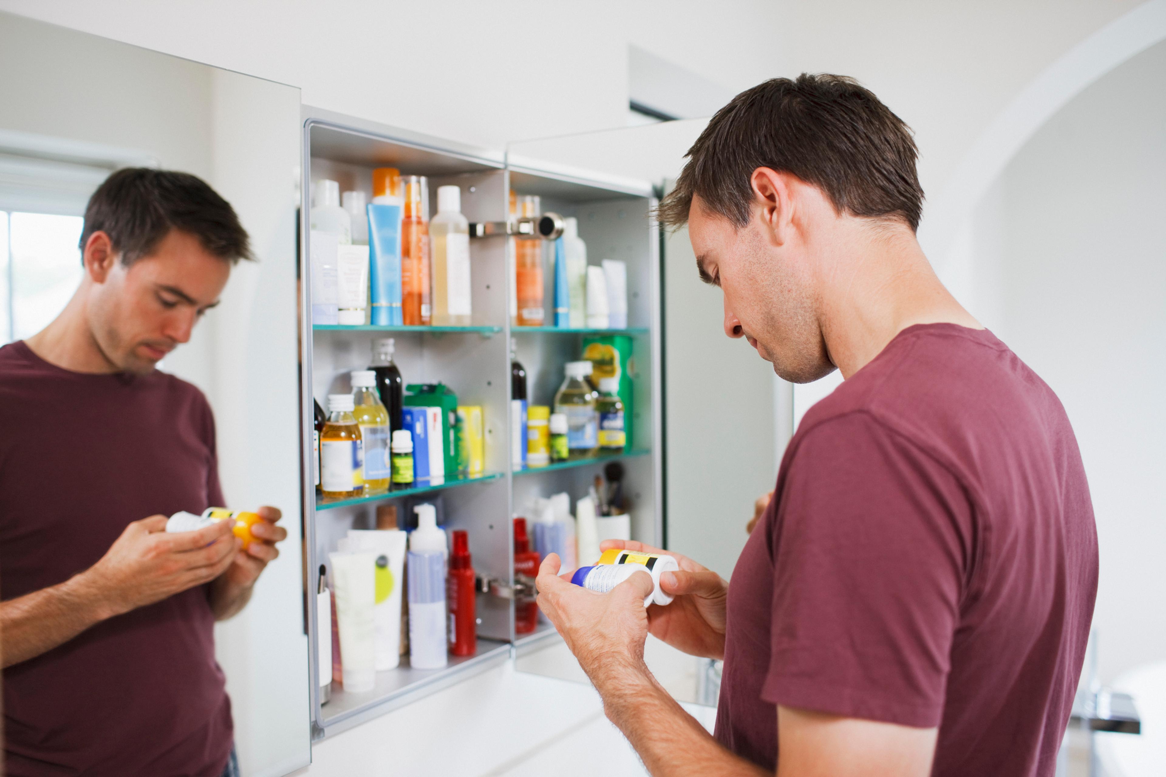 Man looks through prescription medications in his medicine cabinet looking for opioids