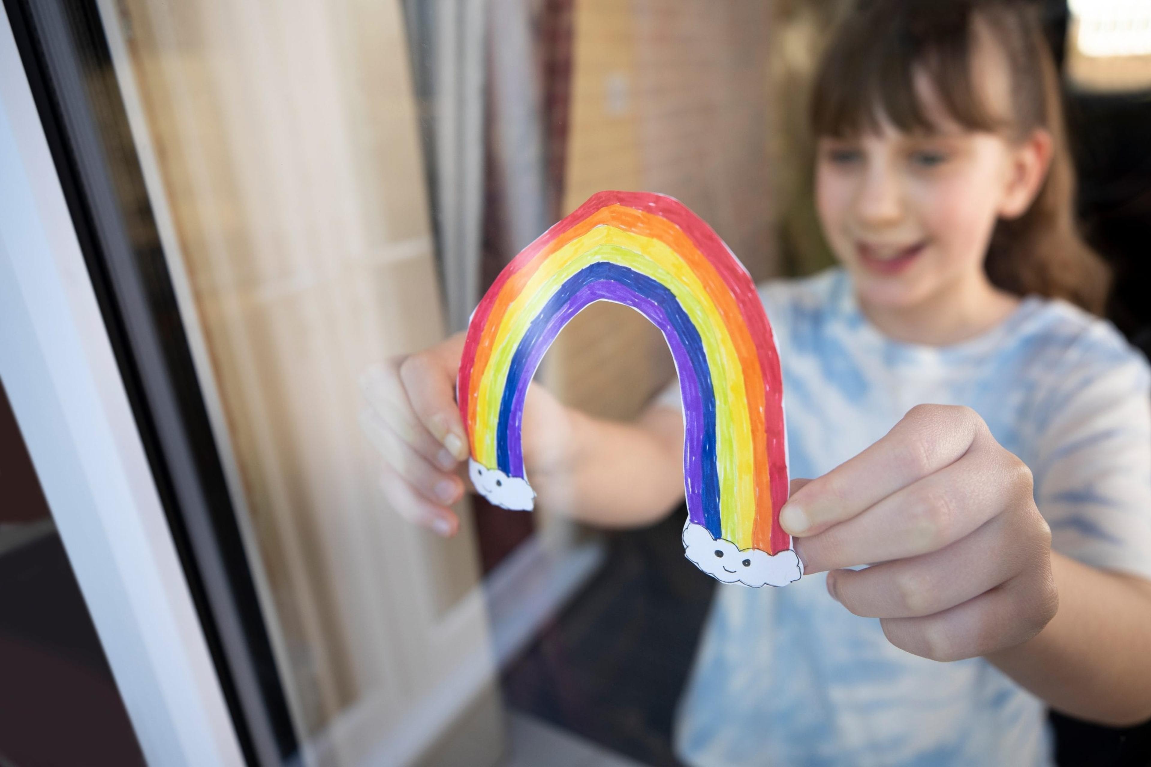 Girl putting a rainbow on her front door.