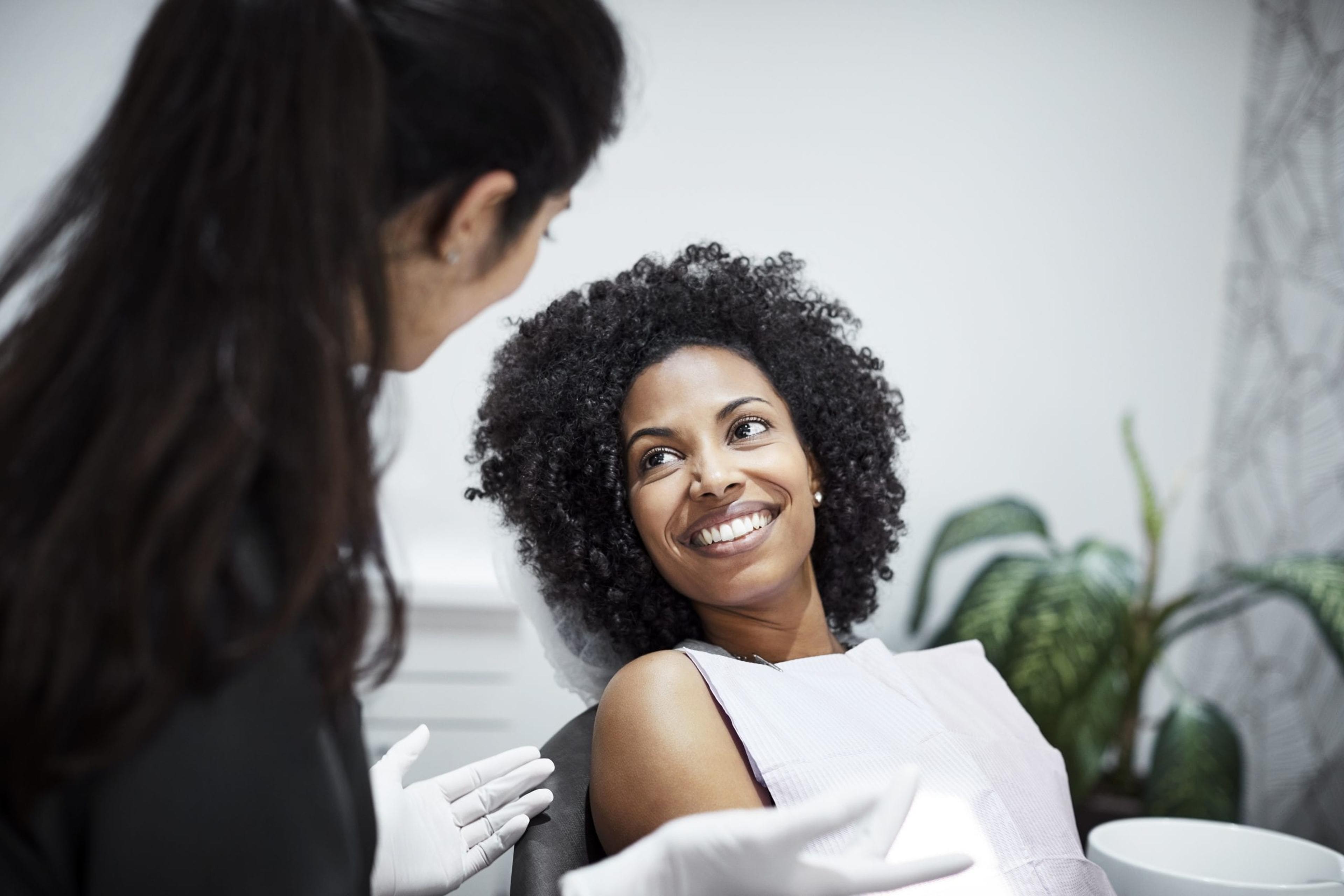 Smiling woman listening to dental doctor. Female dentist is discussing with patient. They are in clinic.