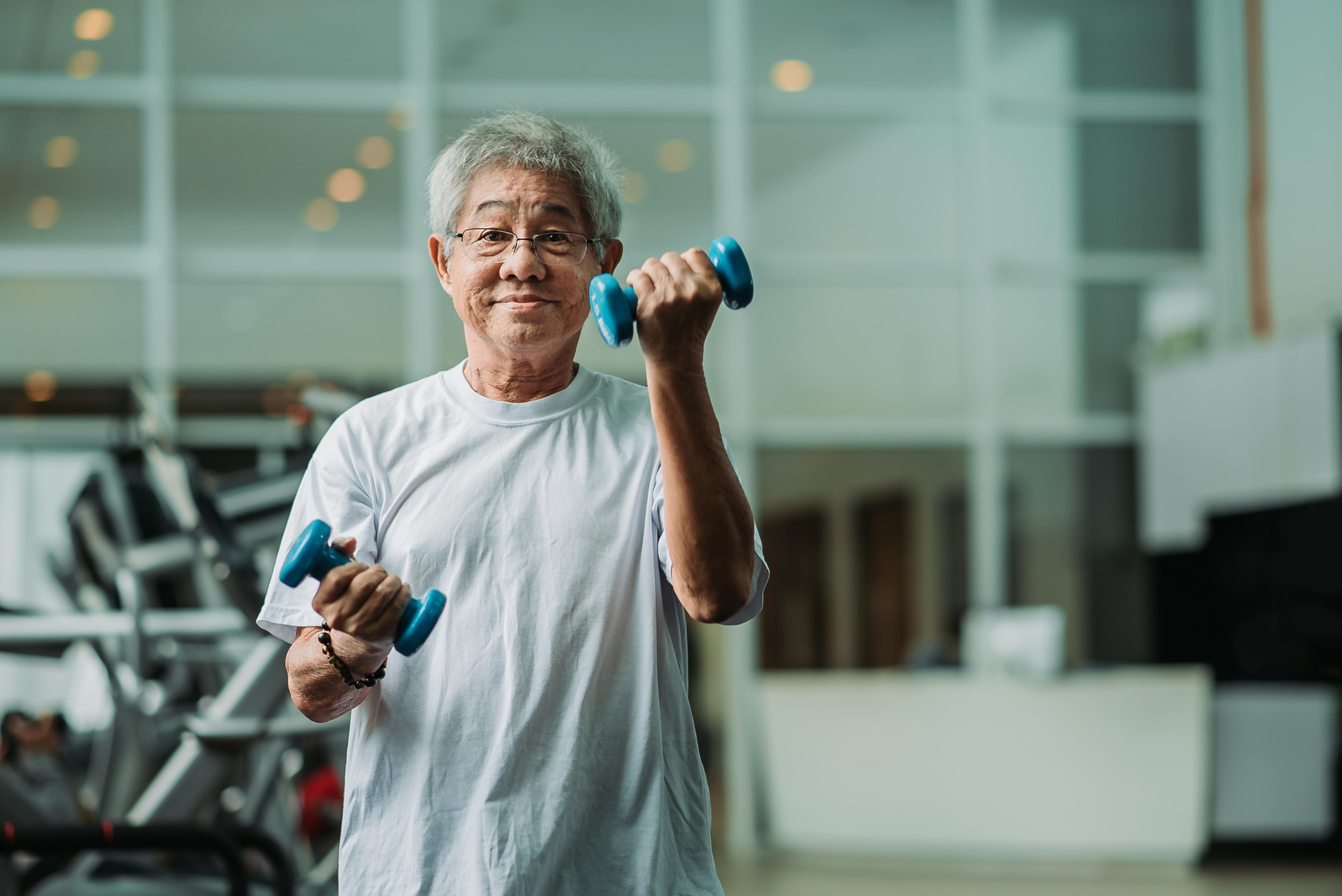 Asian active senior male exercising and workout with dumbbell in gym room during weekend activity