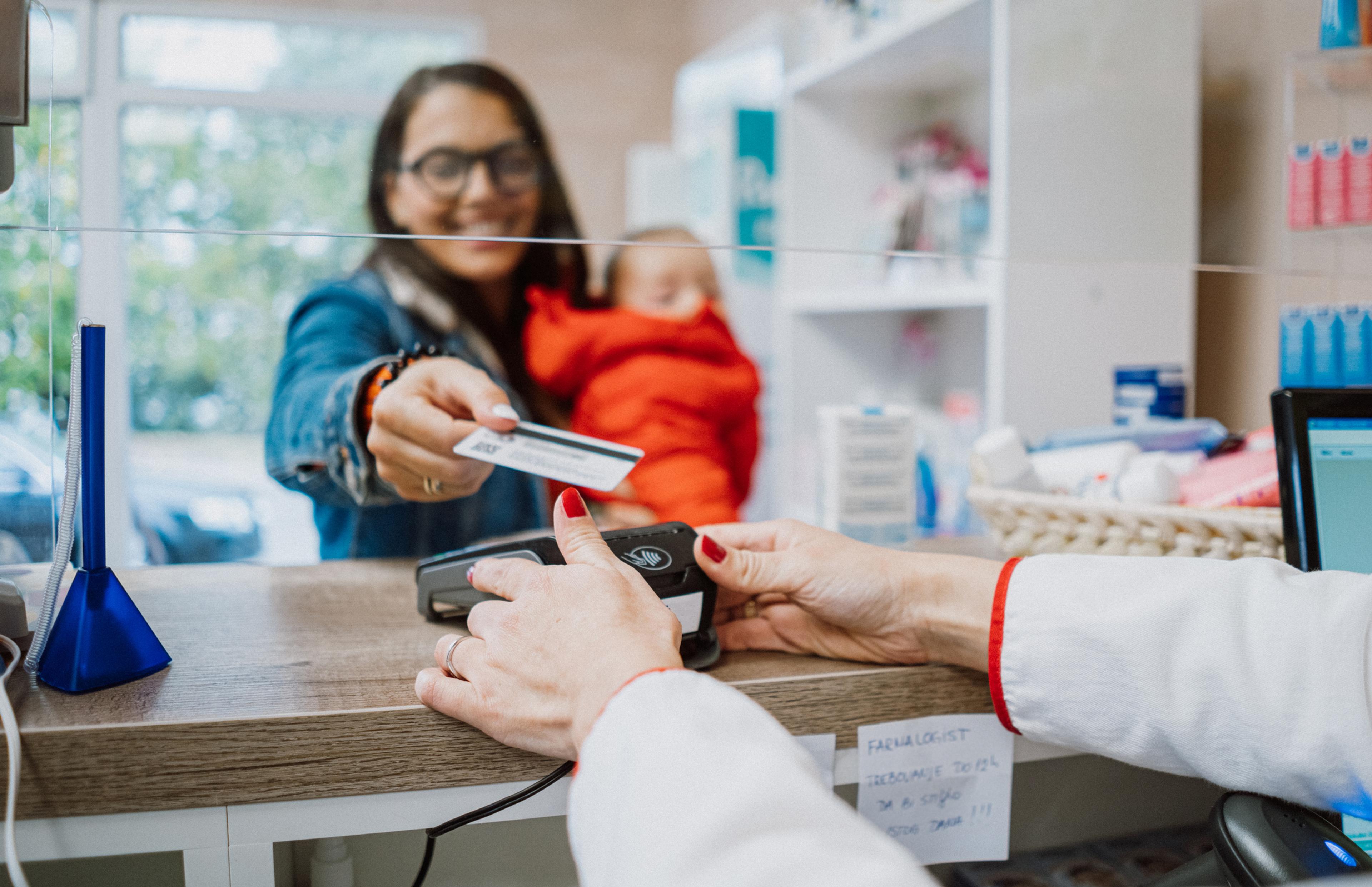 A woman holds her baby as she pays for an item at a medical facility.