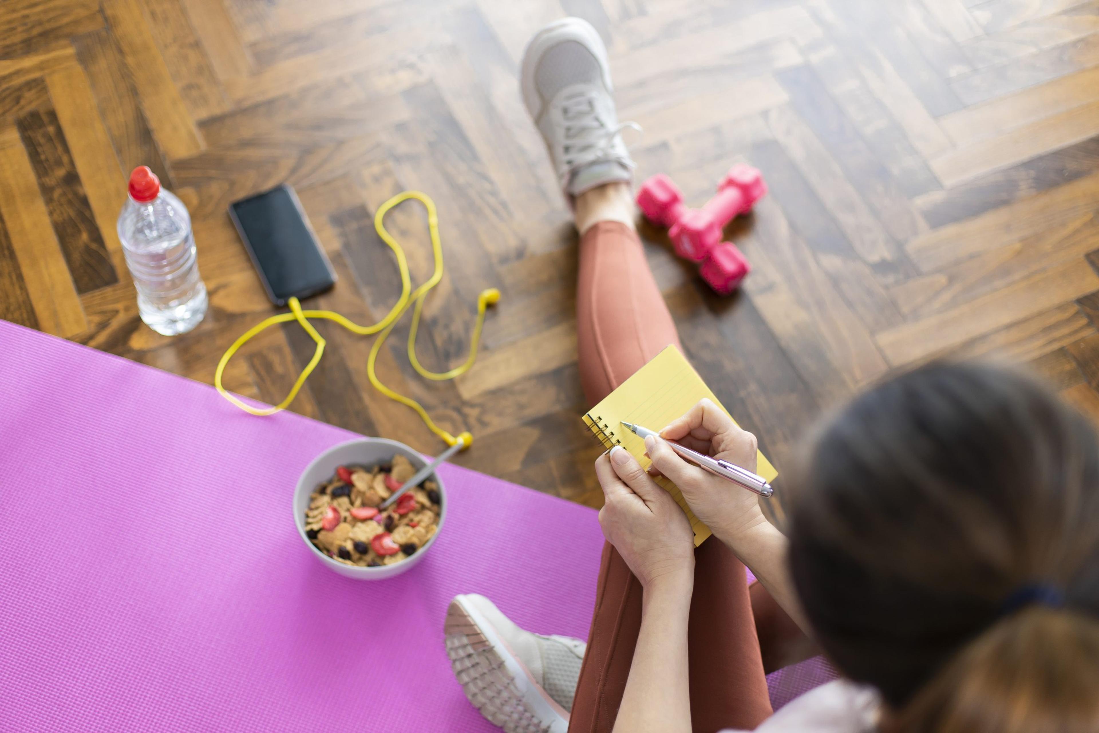 Young sporty woman writing workout plan in notebook after a workout