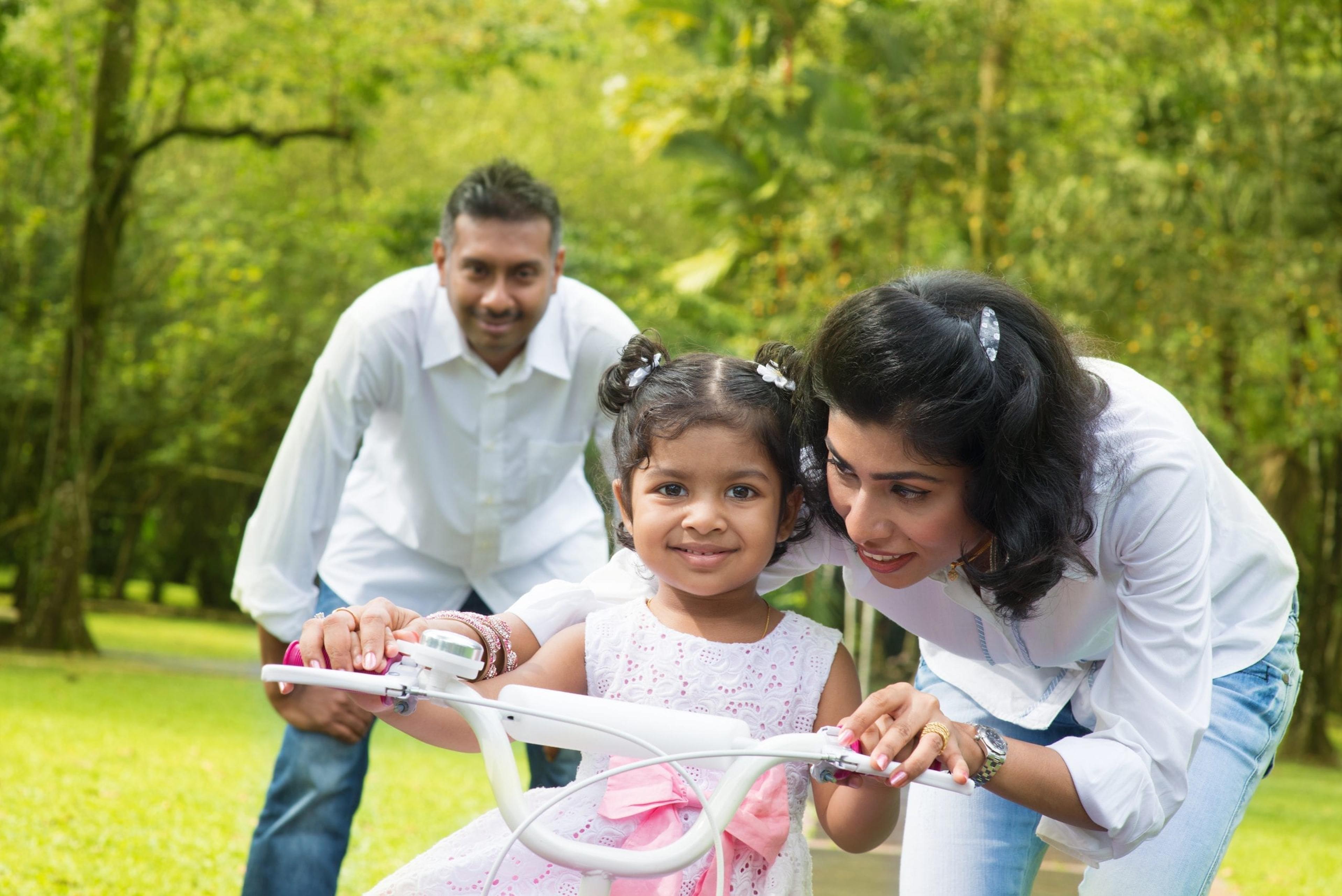 Mom and dad helping little girl learn to ride a bike