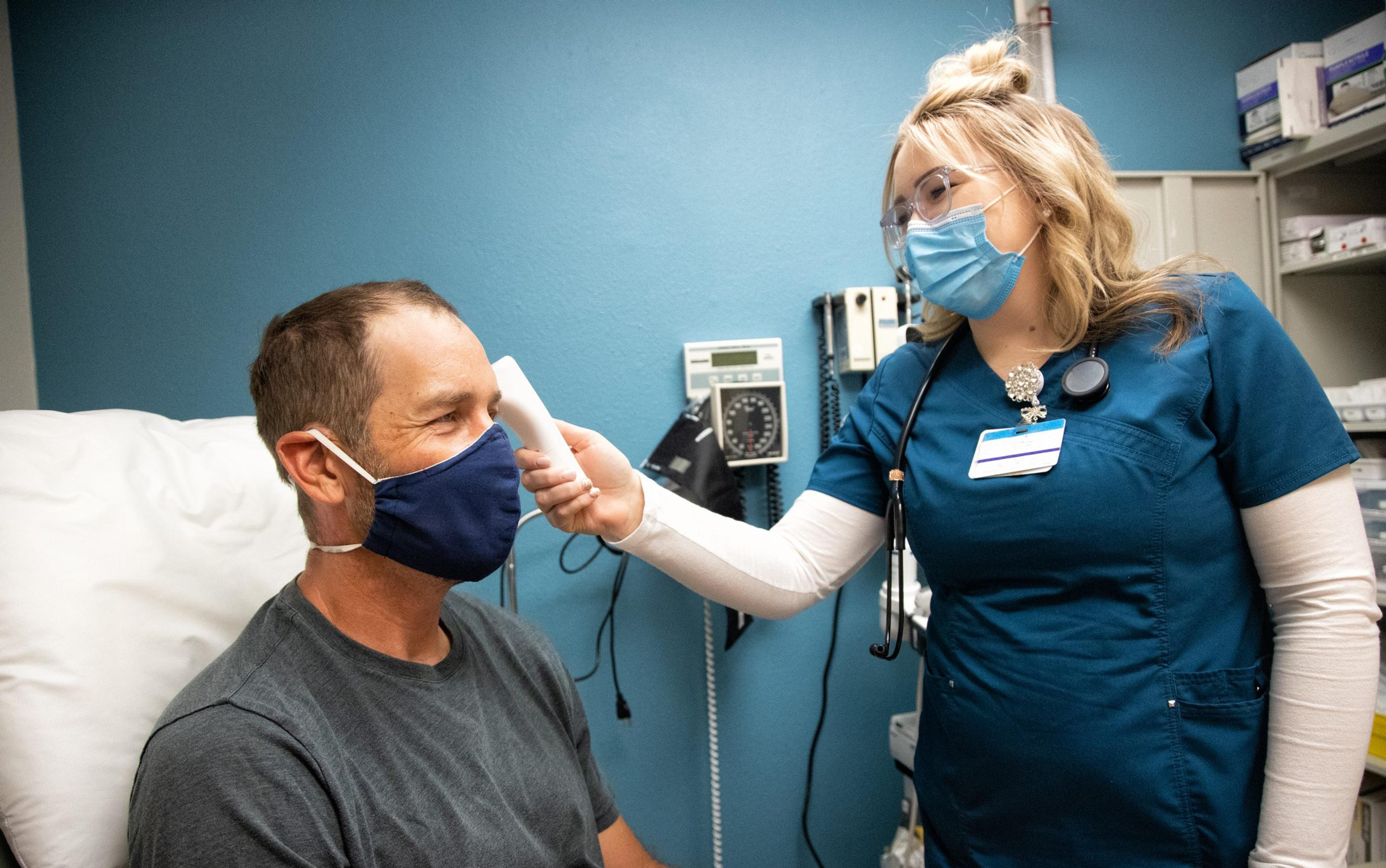Nurse wearing a mask takes the temperature using a forehead thermometer