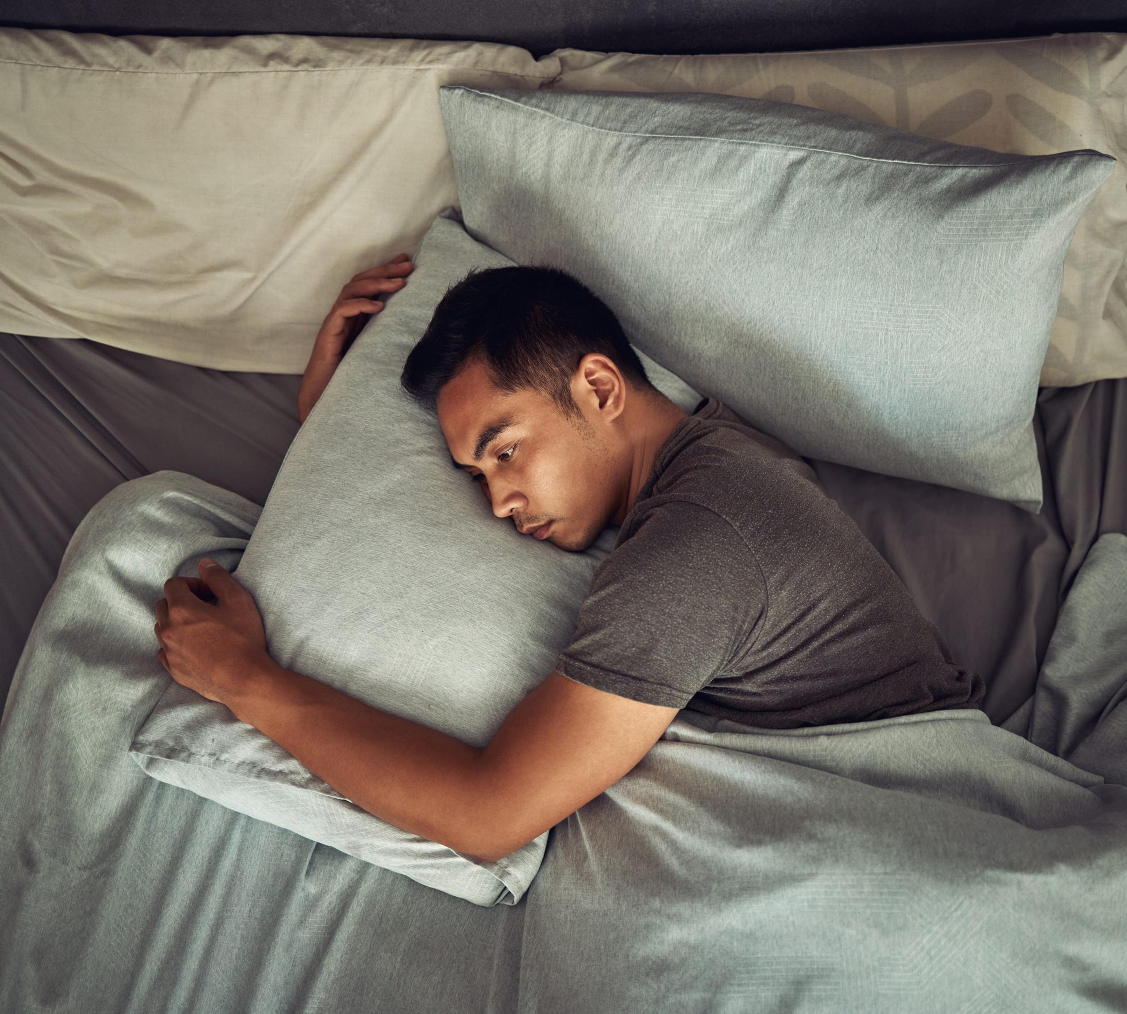 Man lying in bed hugging his pillow, trying to sleep