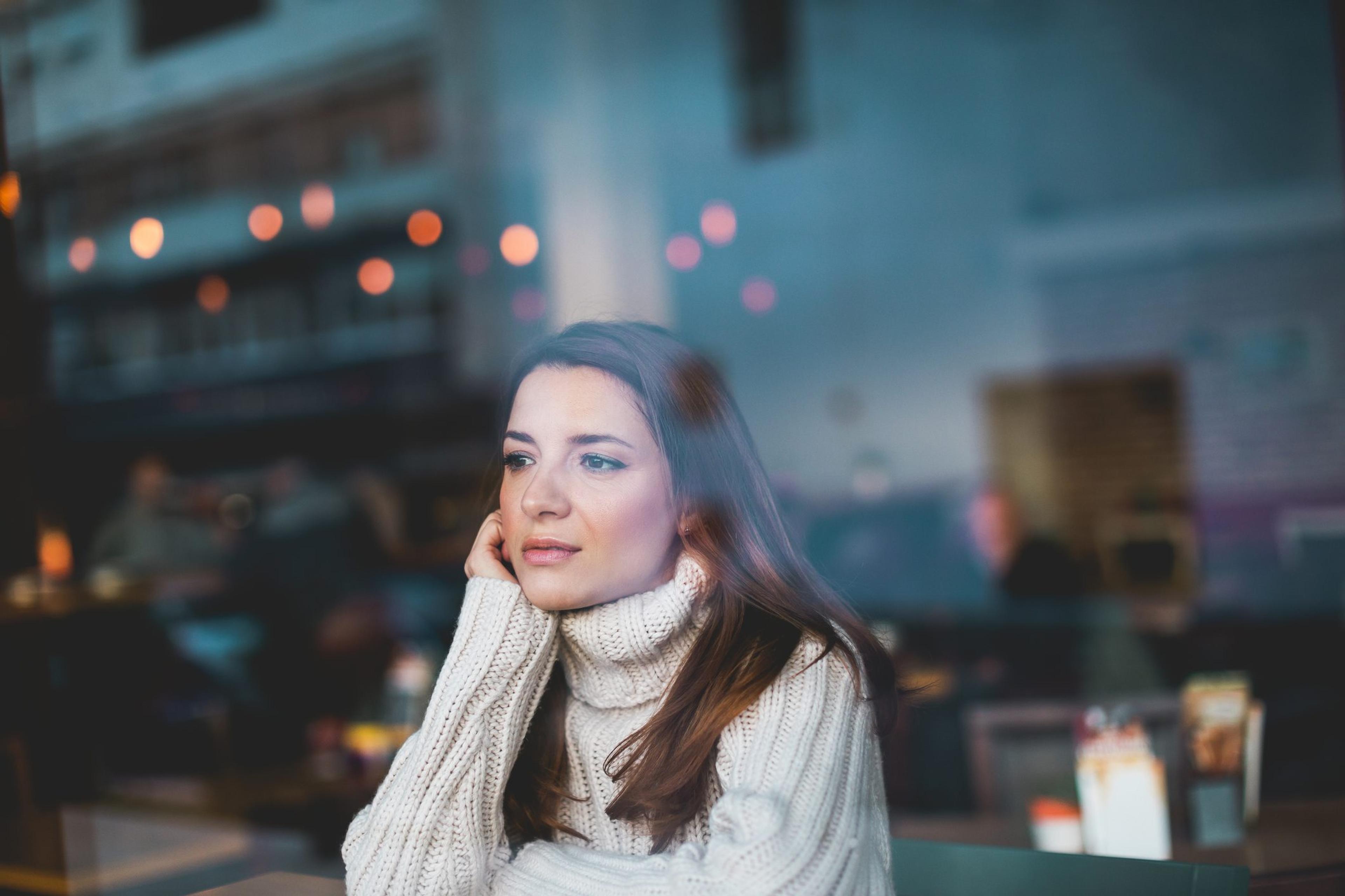 Woman sits alone in a cafe looking out the windows feeling the holiday blues