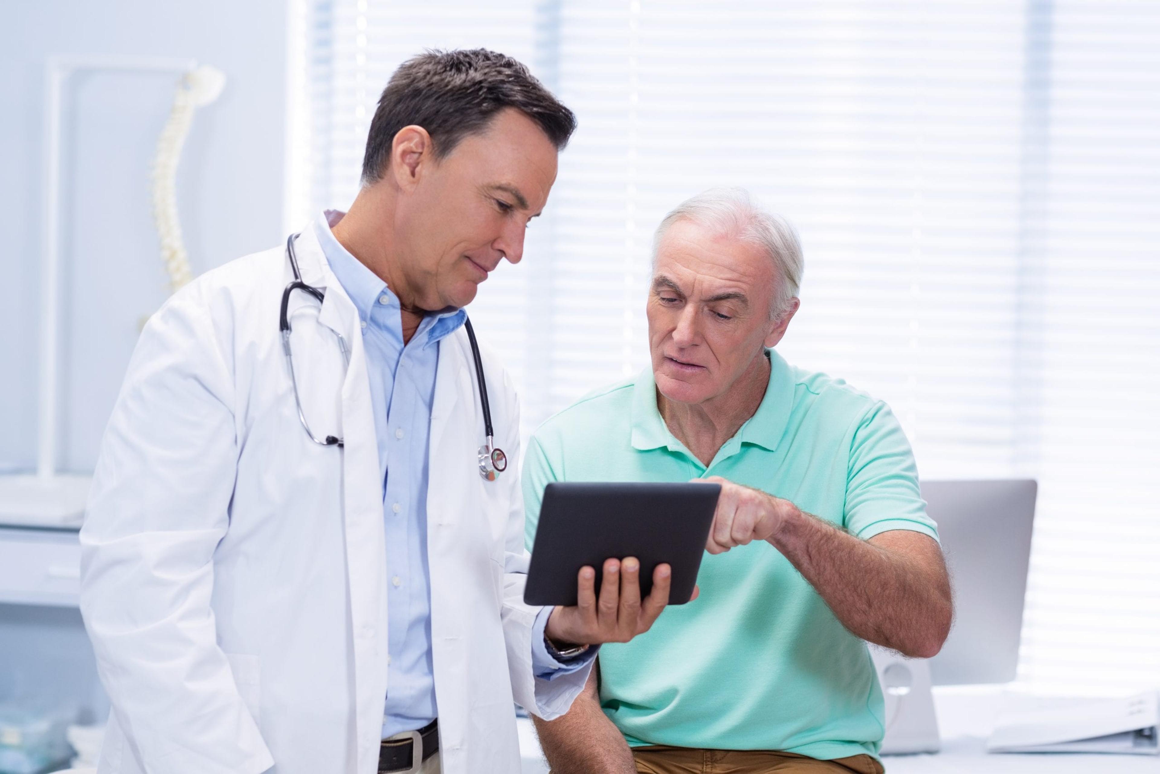 Doctor and senior patient using digital tablet in clinic.