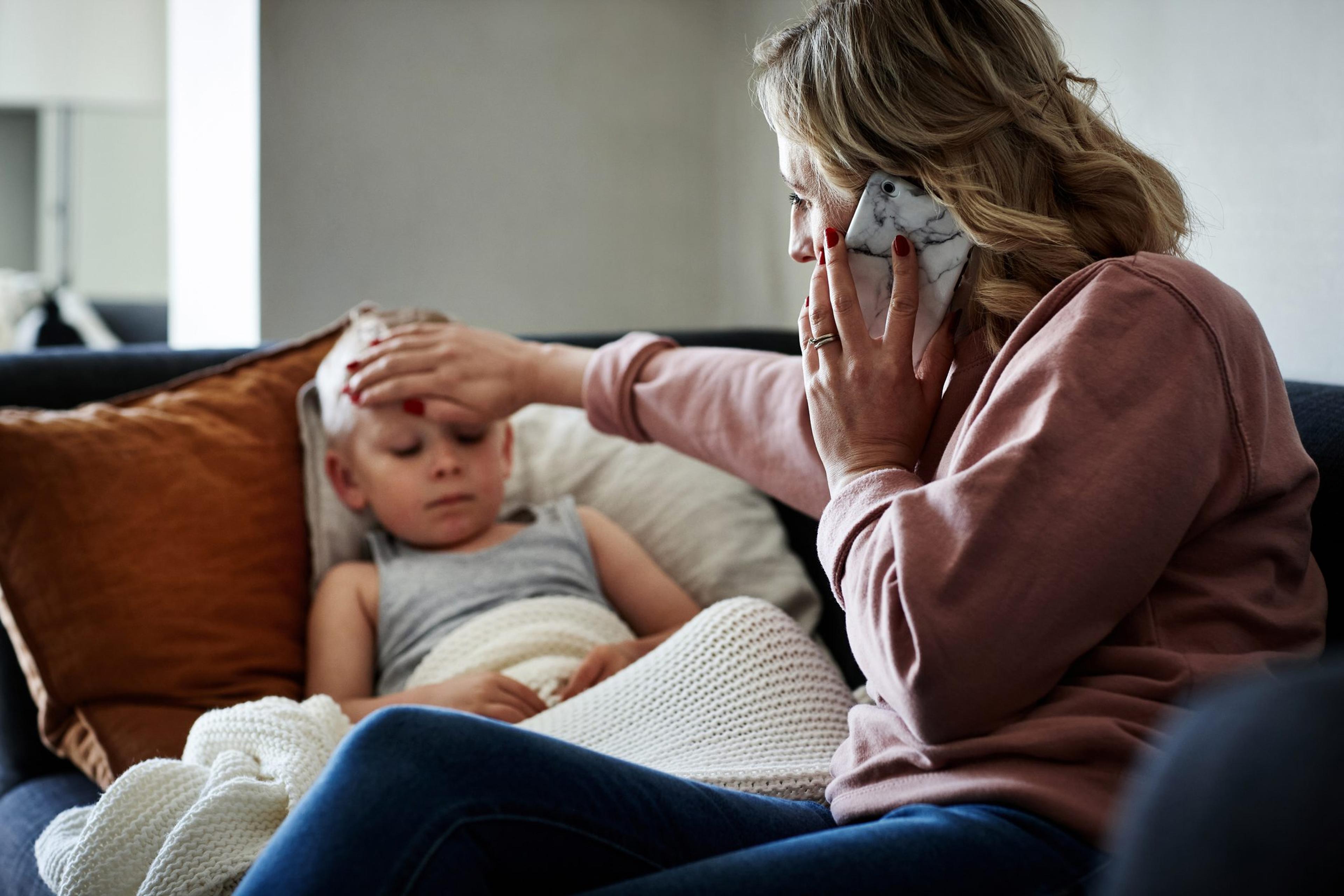 Mother on the phone holding her hand to her sick son's forehead worried about Influenza A