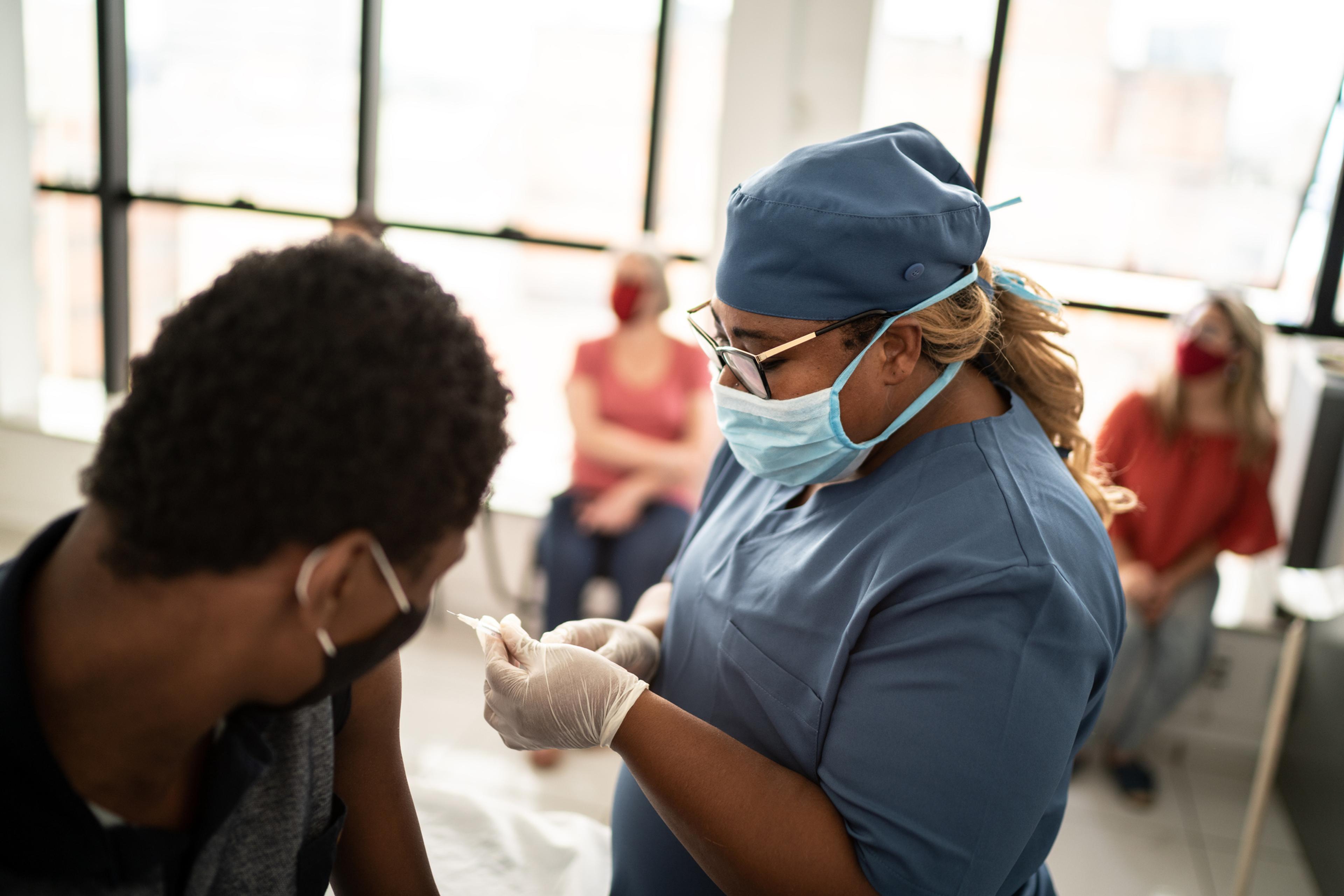 Nurse wearing a mask and gloves gives a boy a booster shot of a vaccine