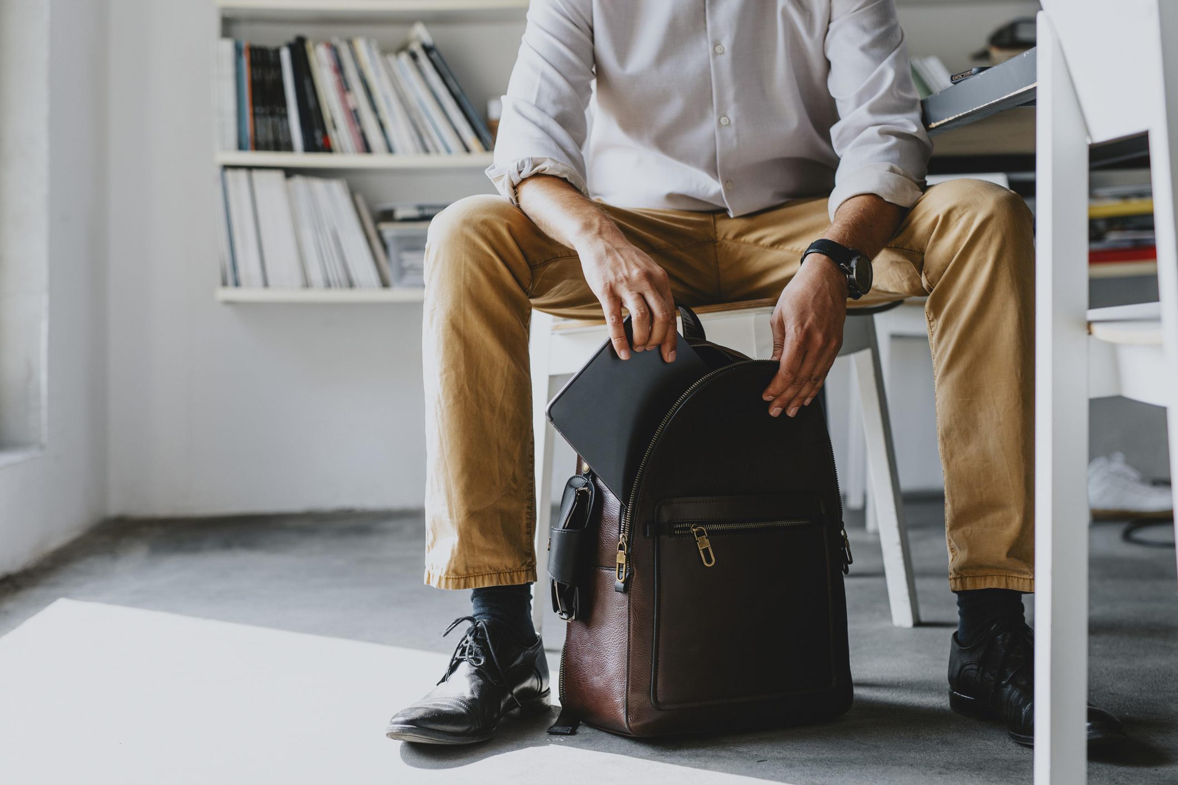 Business man putting a laptop into a backpack