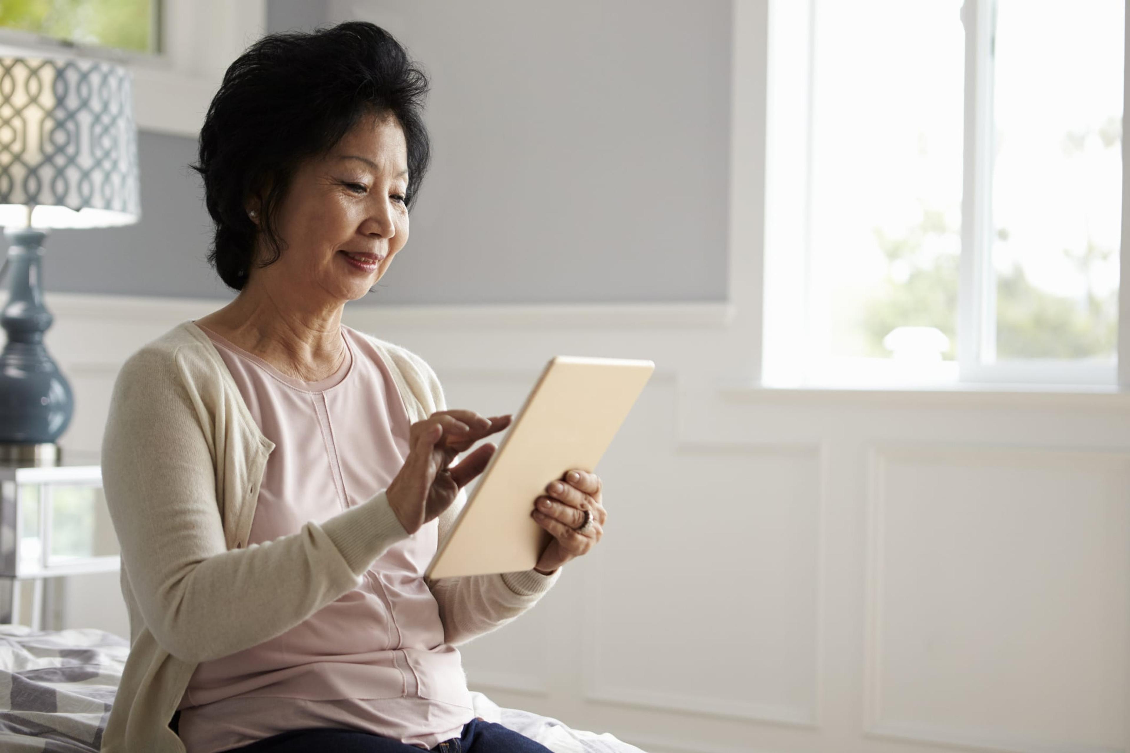senior woman sitting on bed using tablet