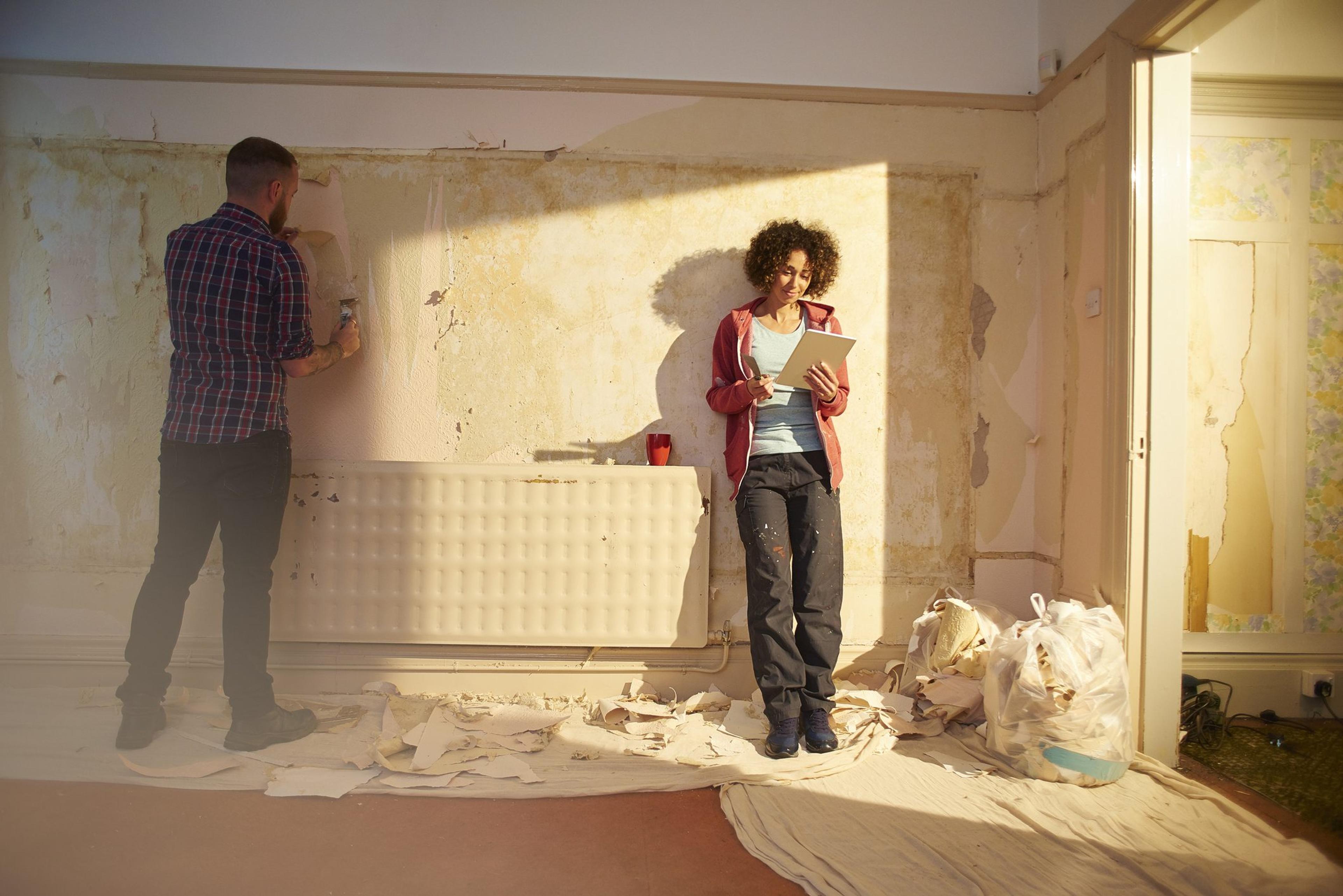 A couple is scraping paint off a wall in an old home