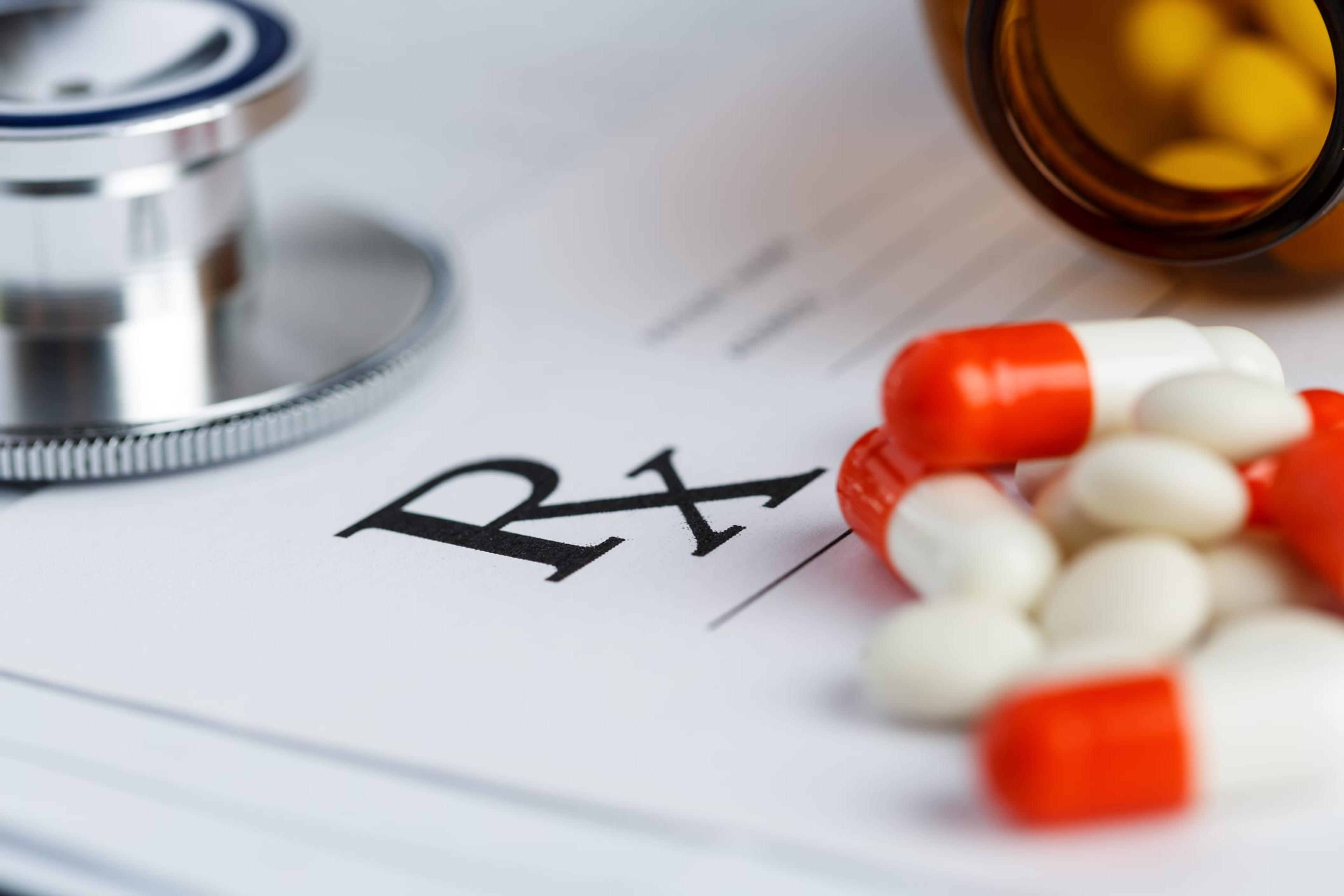 Prescription form lying on table with stethoscope, pen and pile of pills fell out from jar. Empty medical form ready to be used.