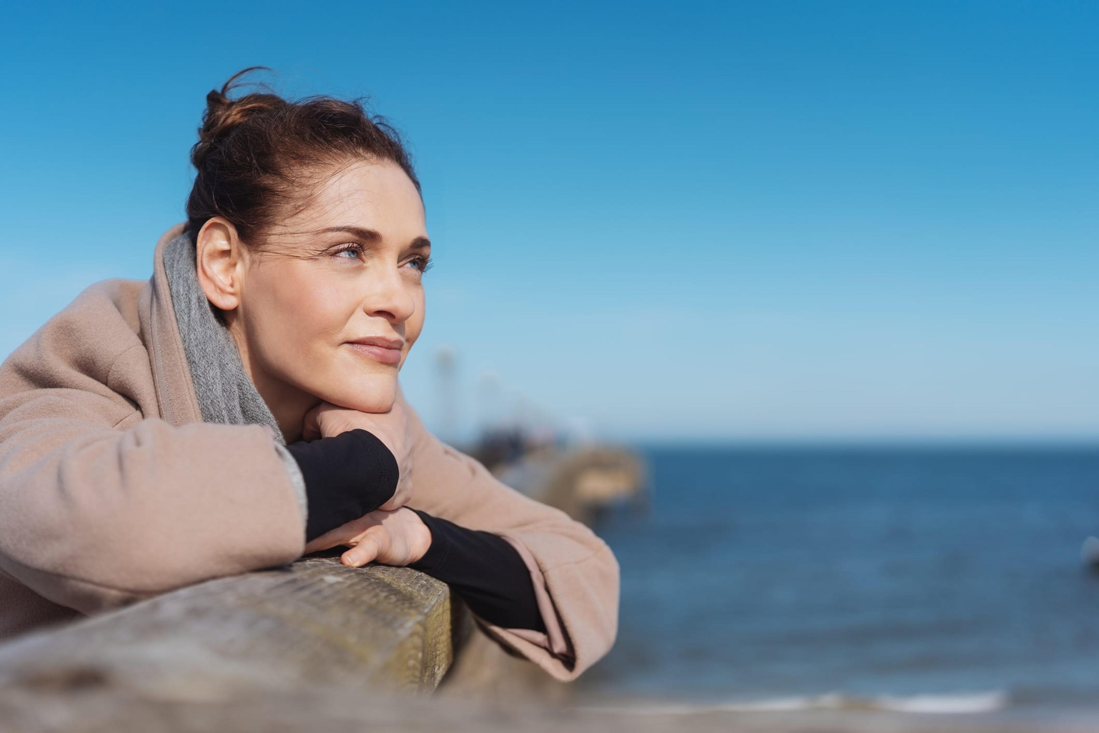 A woman dealing with stress and anxiety leaning over a pier and staring off into the distance