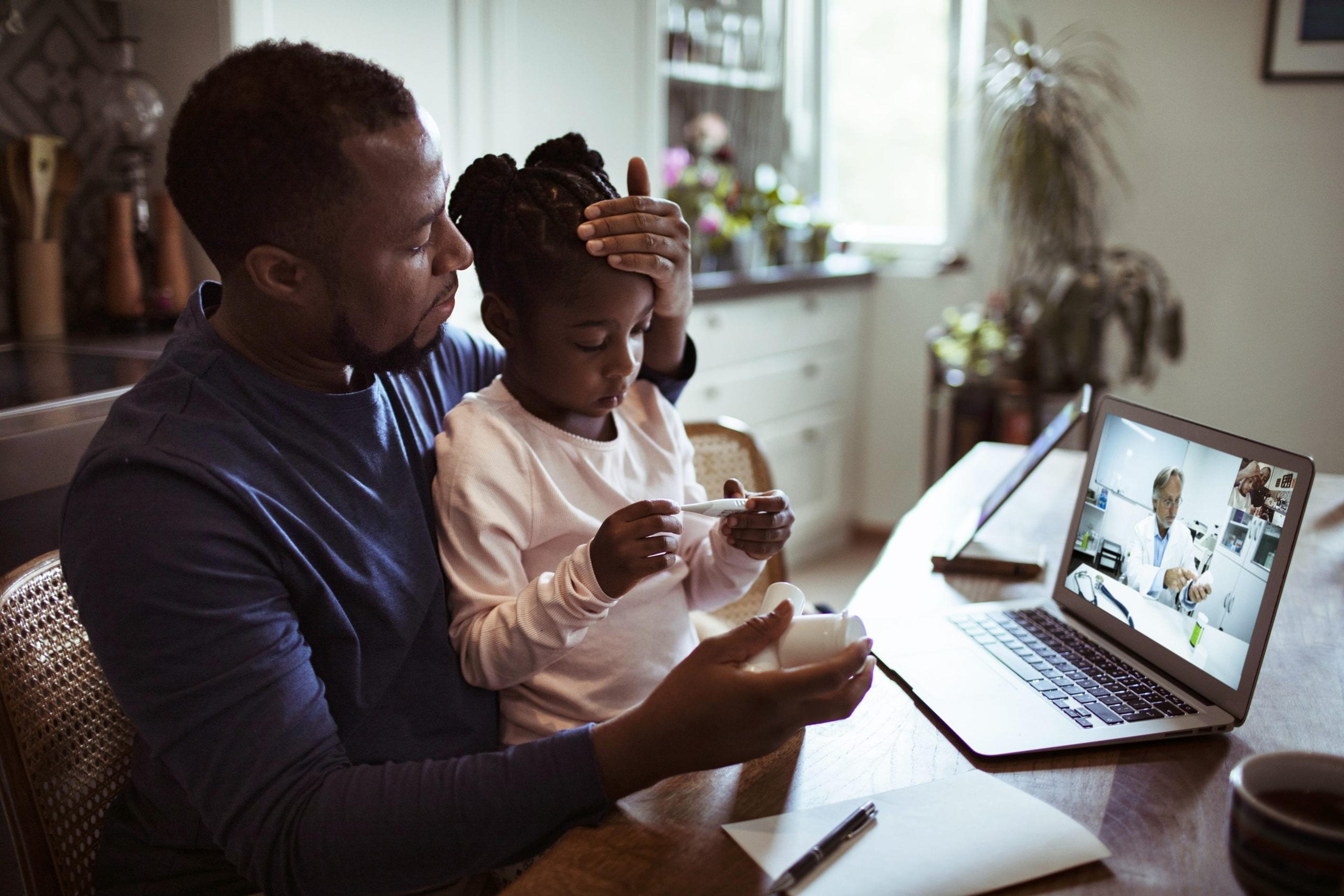 Dad taking his daughter's temperature talking to a doctor online