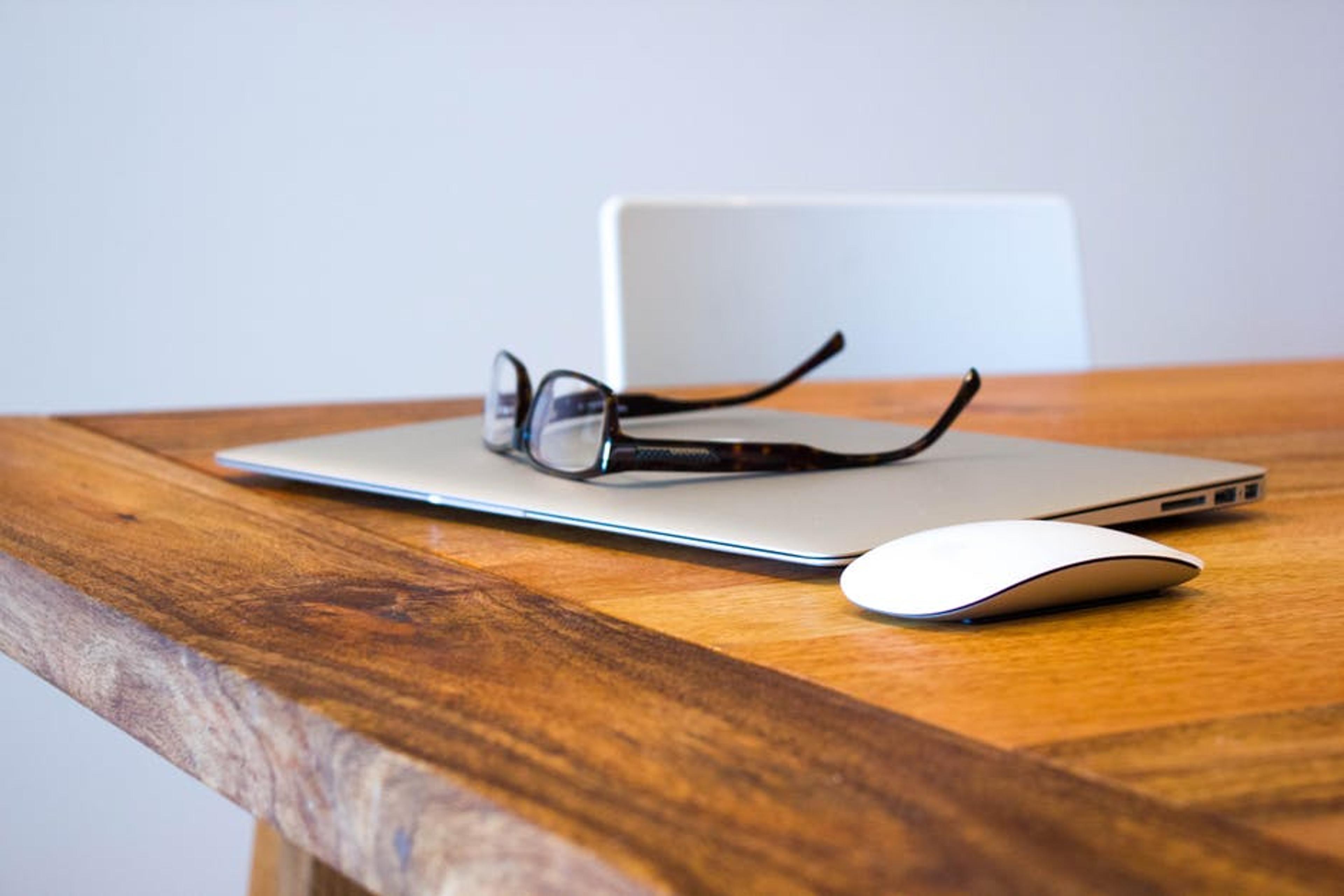 Laptop and mouse sitting on a table. Glasses sitting on top of the closed laptop.