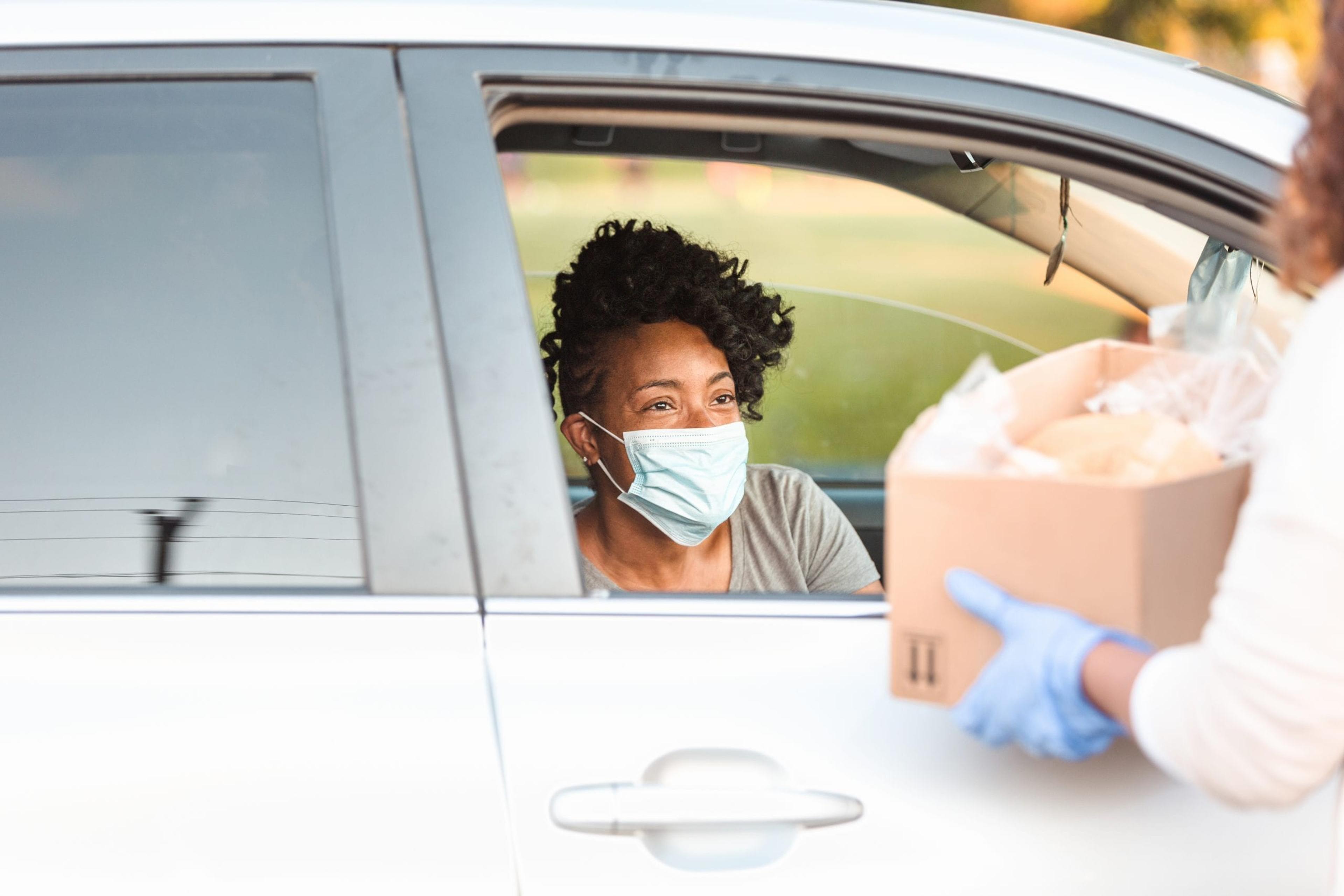 Woman with a mask pulling up to food distribution event