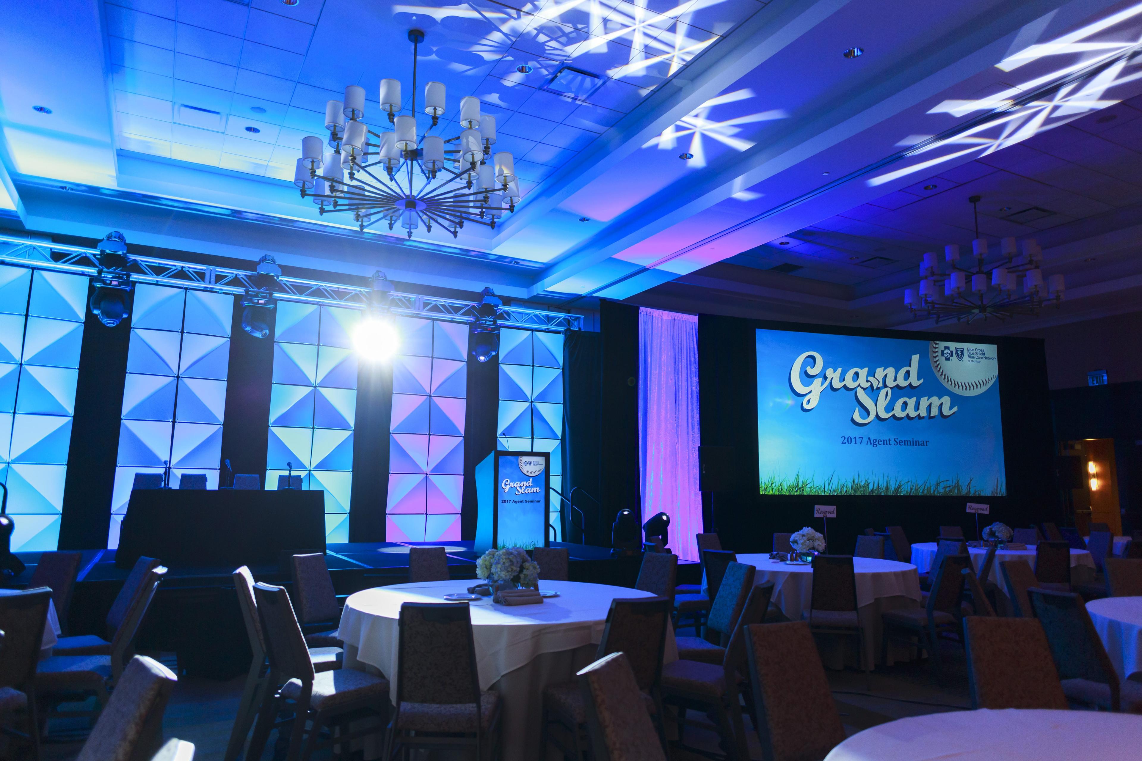 a room with blue lights set up with tables and a stage with a screen