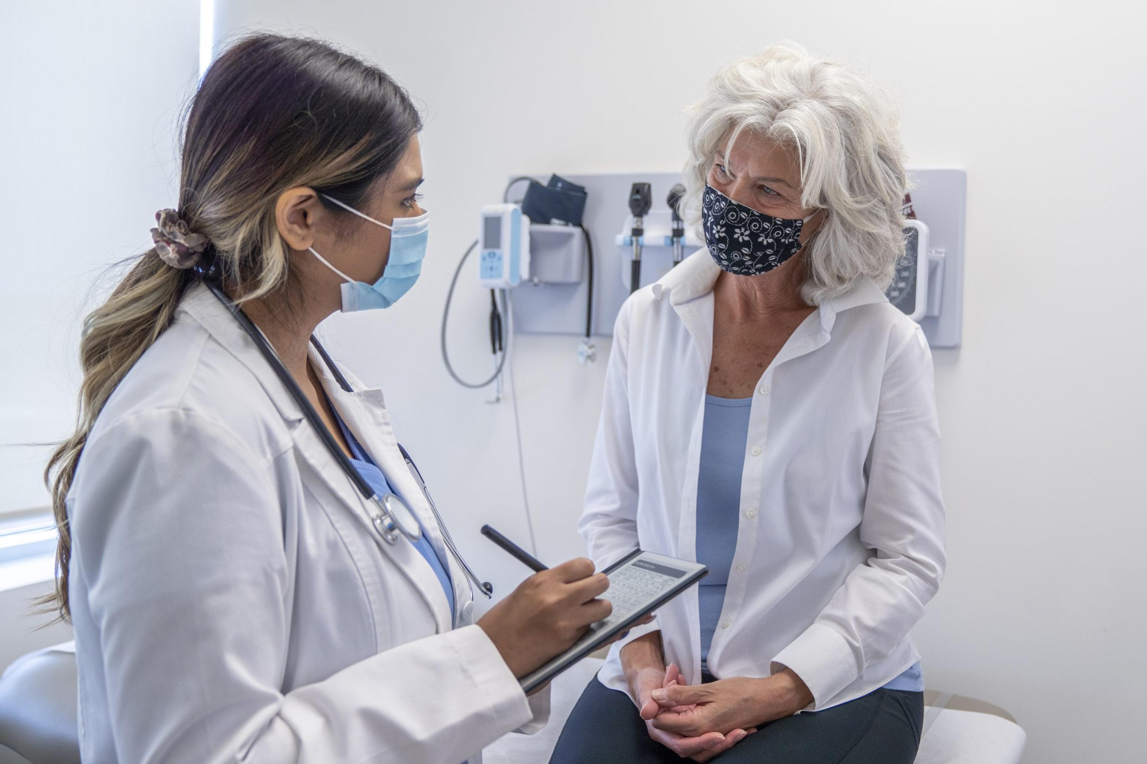 Masked senior woman listening to her doctor during a check up appointment talk about pain scale