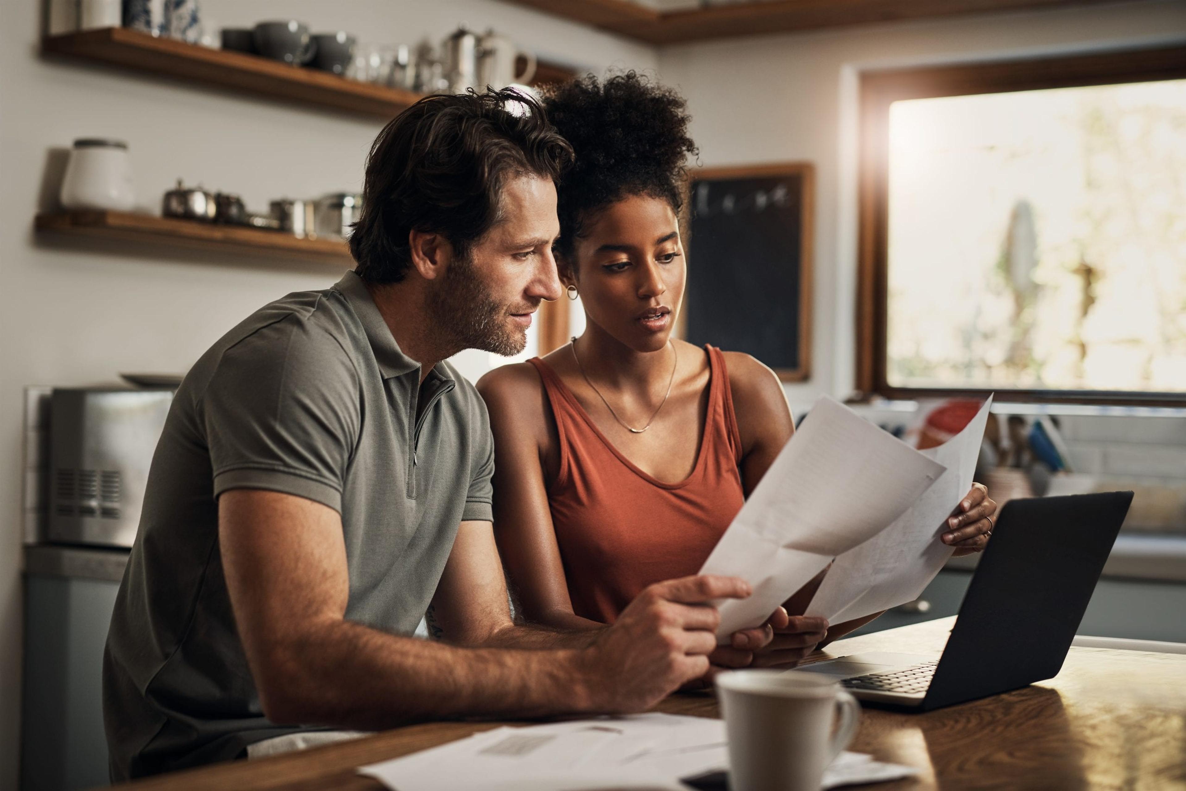 Middle-aged man, woman sit at a desk discussing papers they are both looking at.