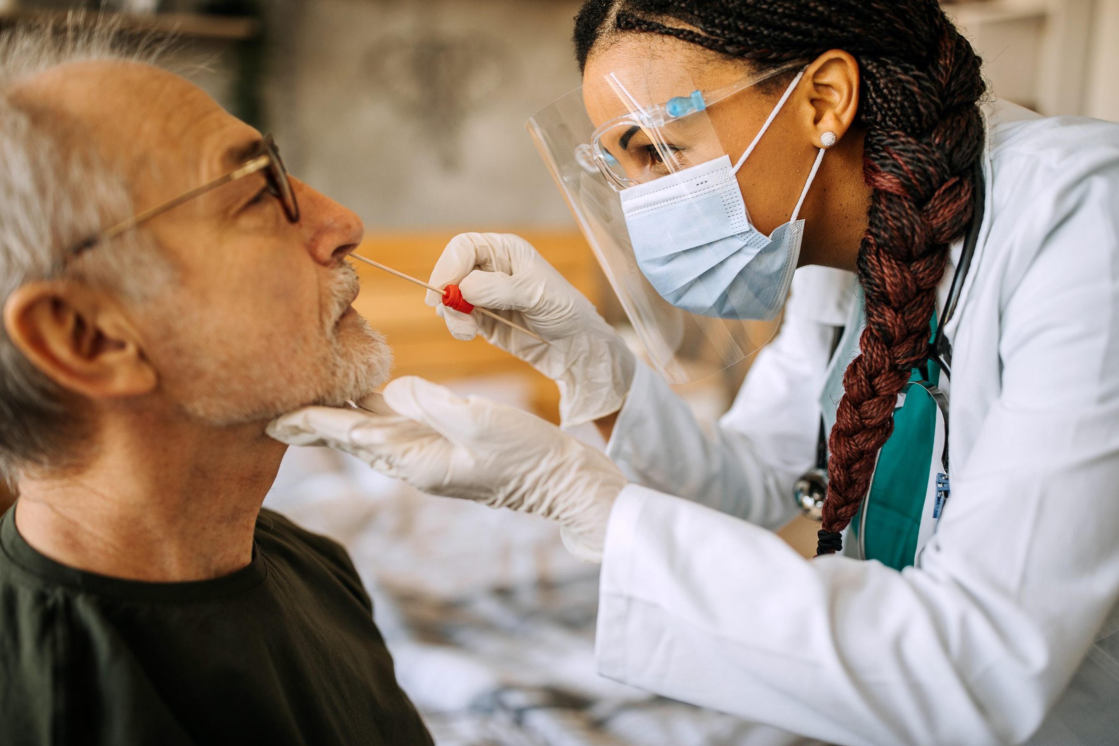 Doctor wearing a mask and gloves tests a man for COVID to see if he is eligible for the new COVID antiviral pill