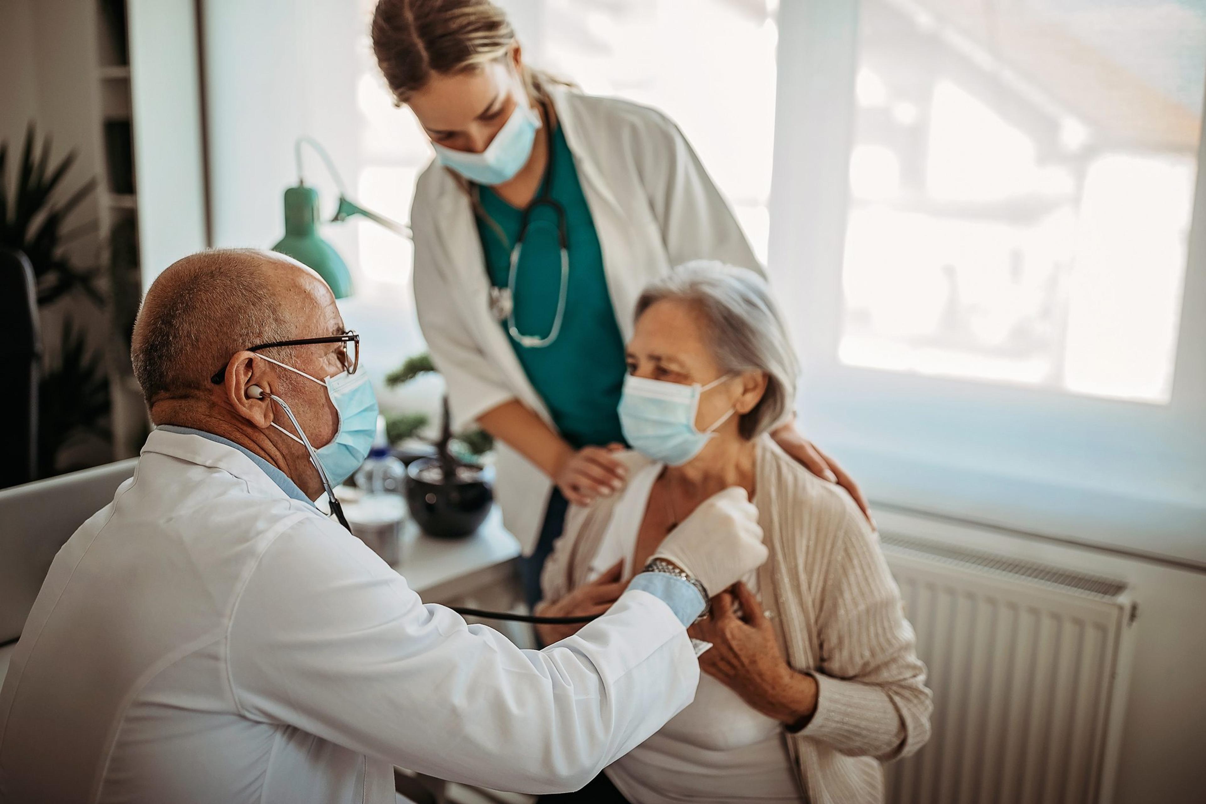 Doctor wearing a mask listens to the heartbeat of an older female patient