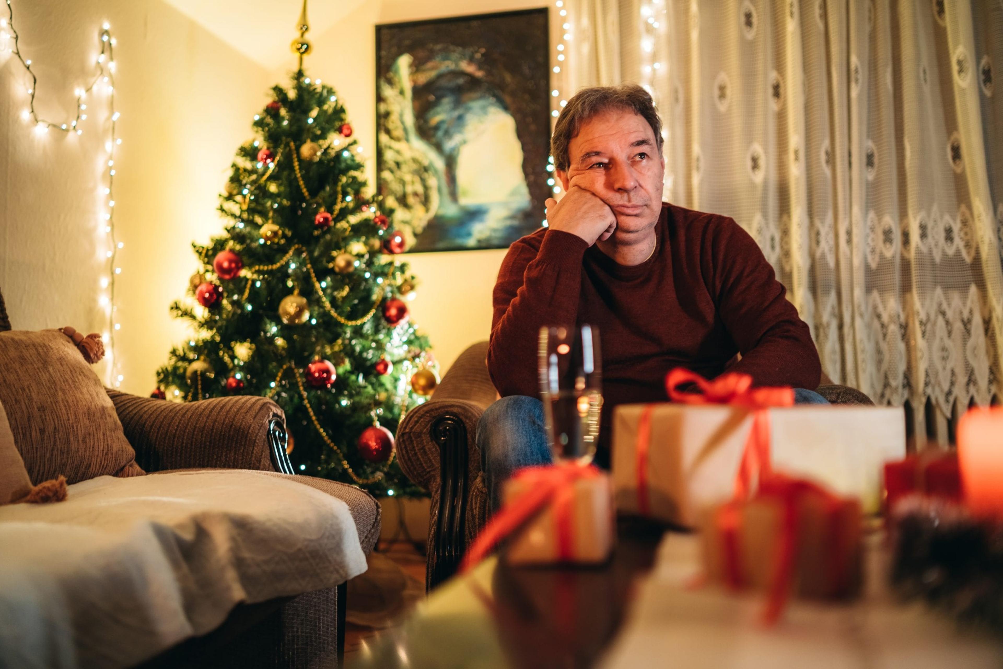 Senior caucasian man sitting on a couch and waiting alone for Christmas / New Year's eve.