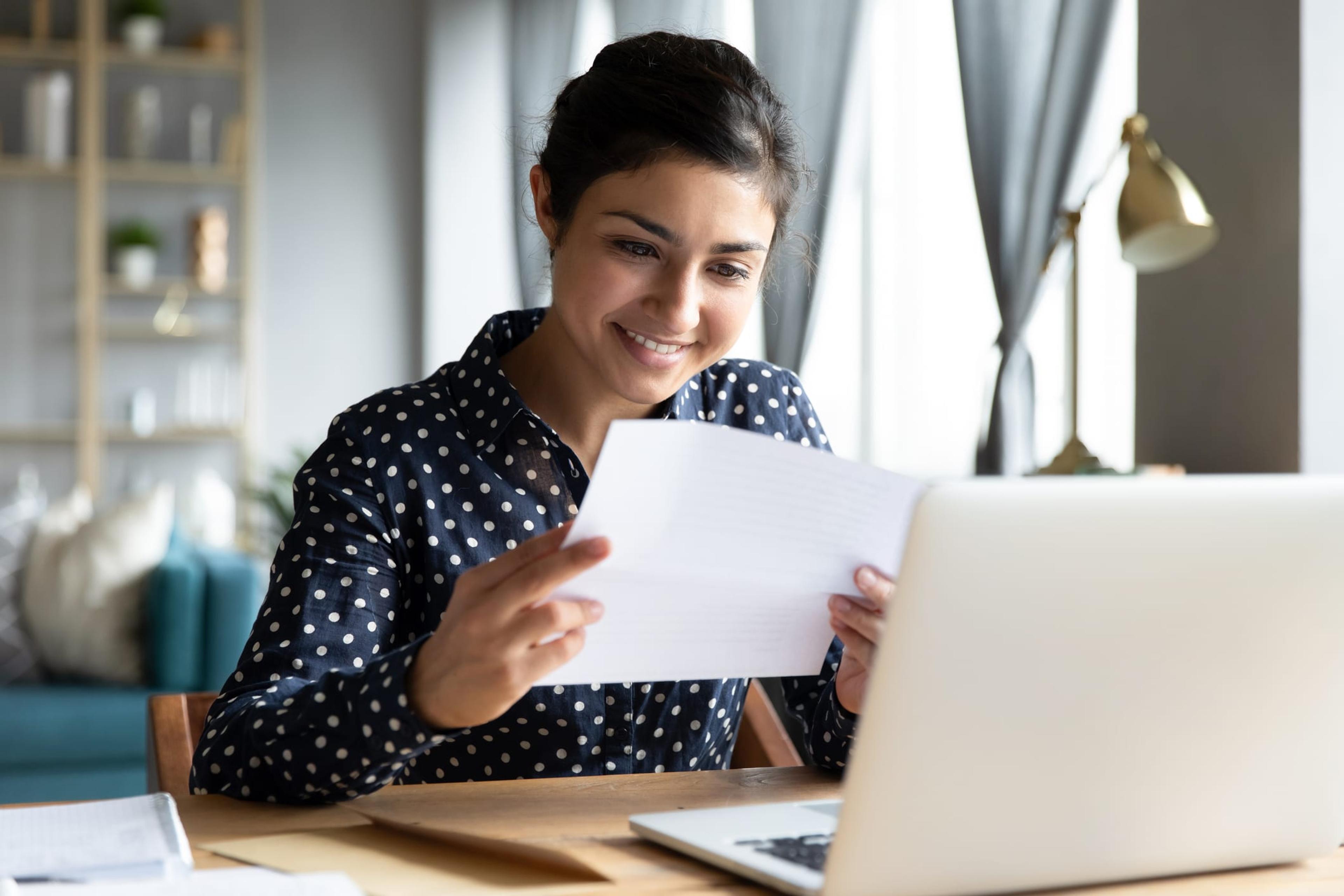 Woman smiling and holding bill in front of laptop