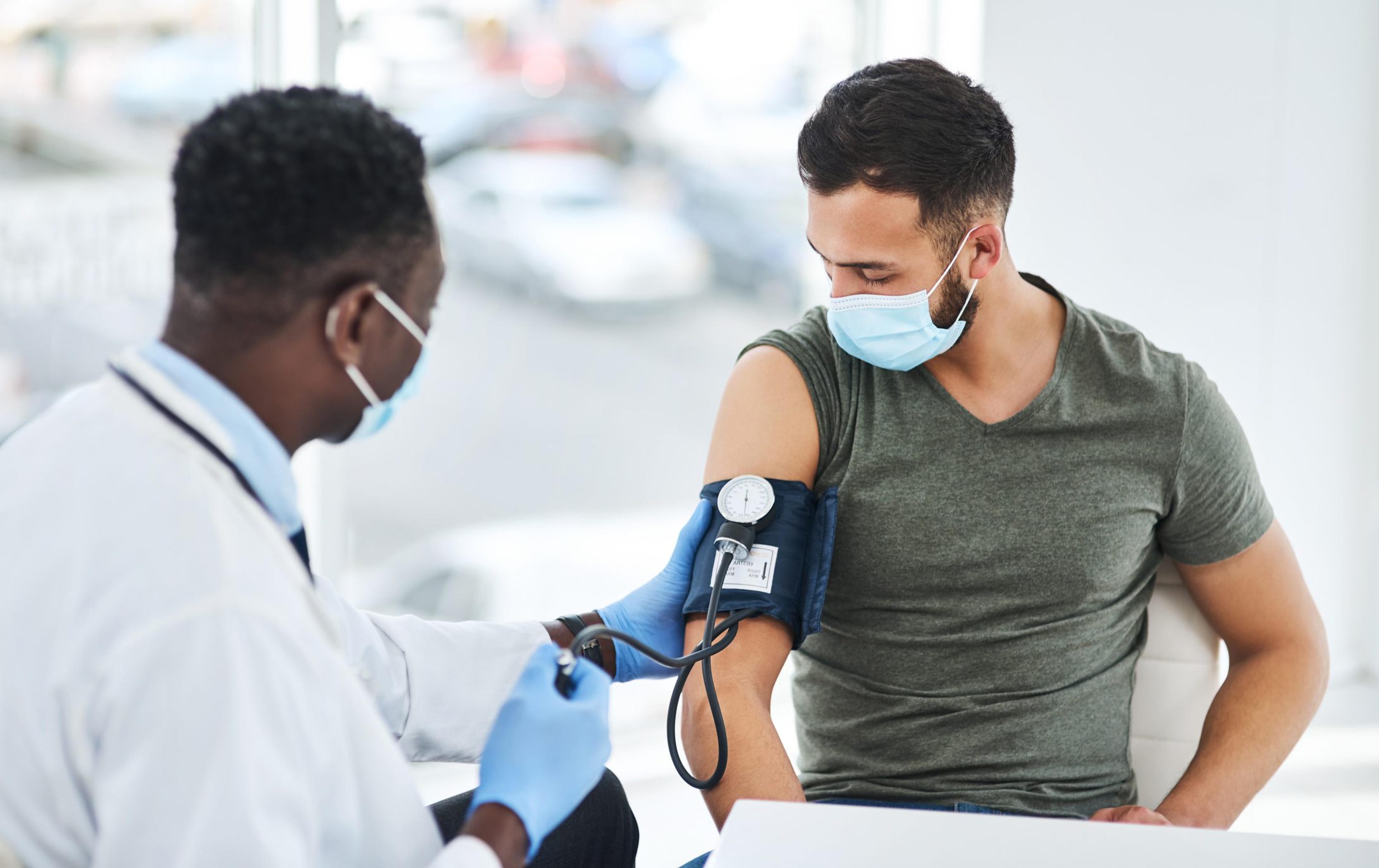 Doctor wearing a mask takes the blood pressure of a young man wearing a mask