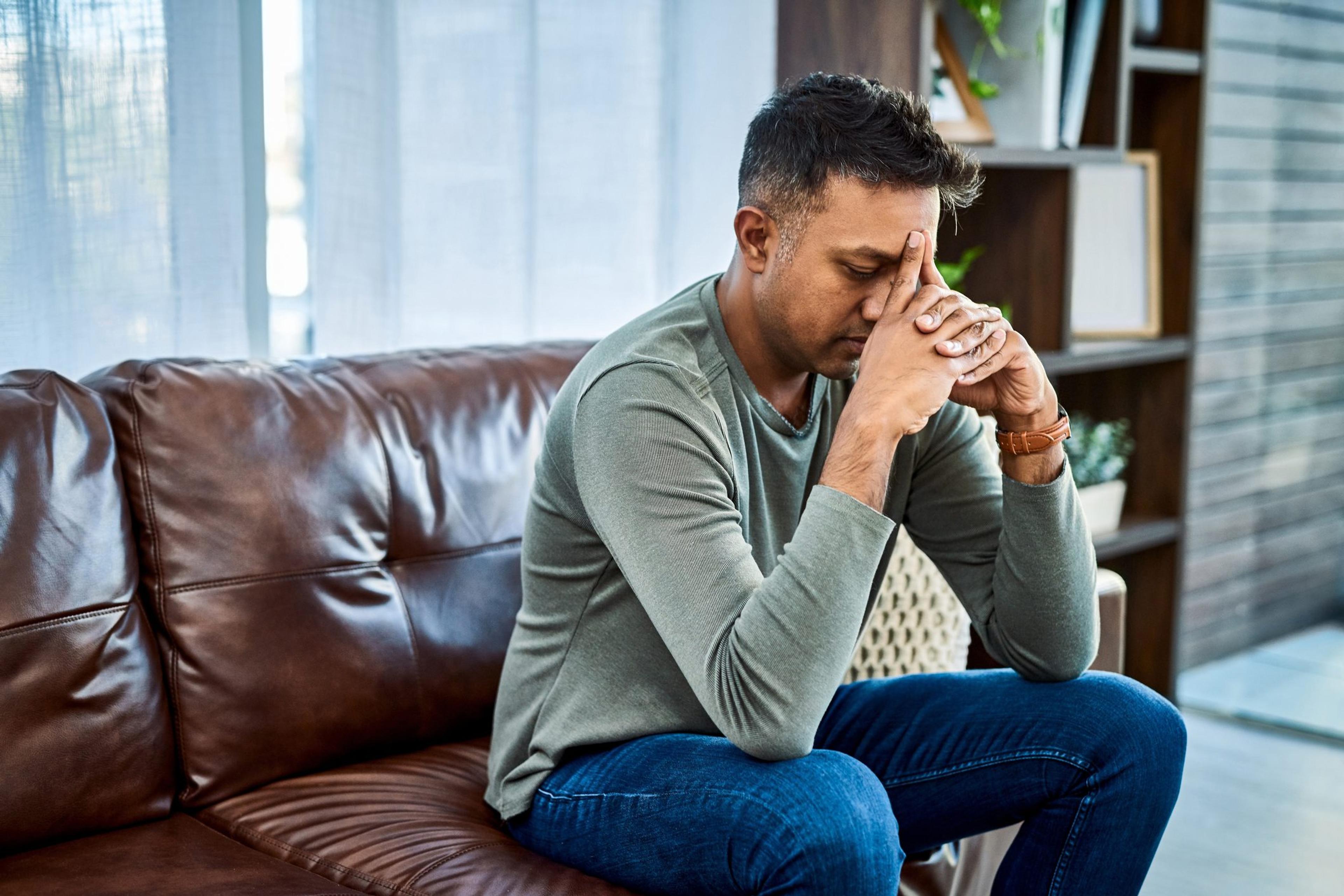 man sitting on a couch with his head in his hands