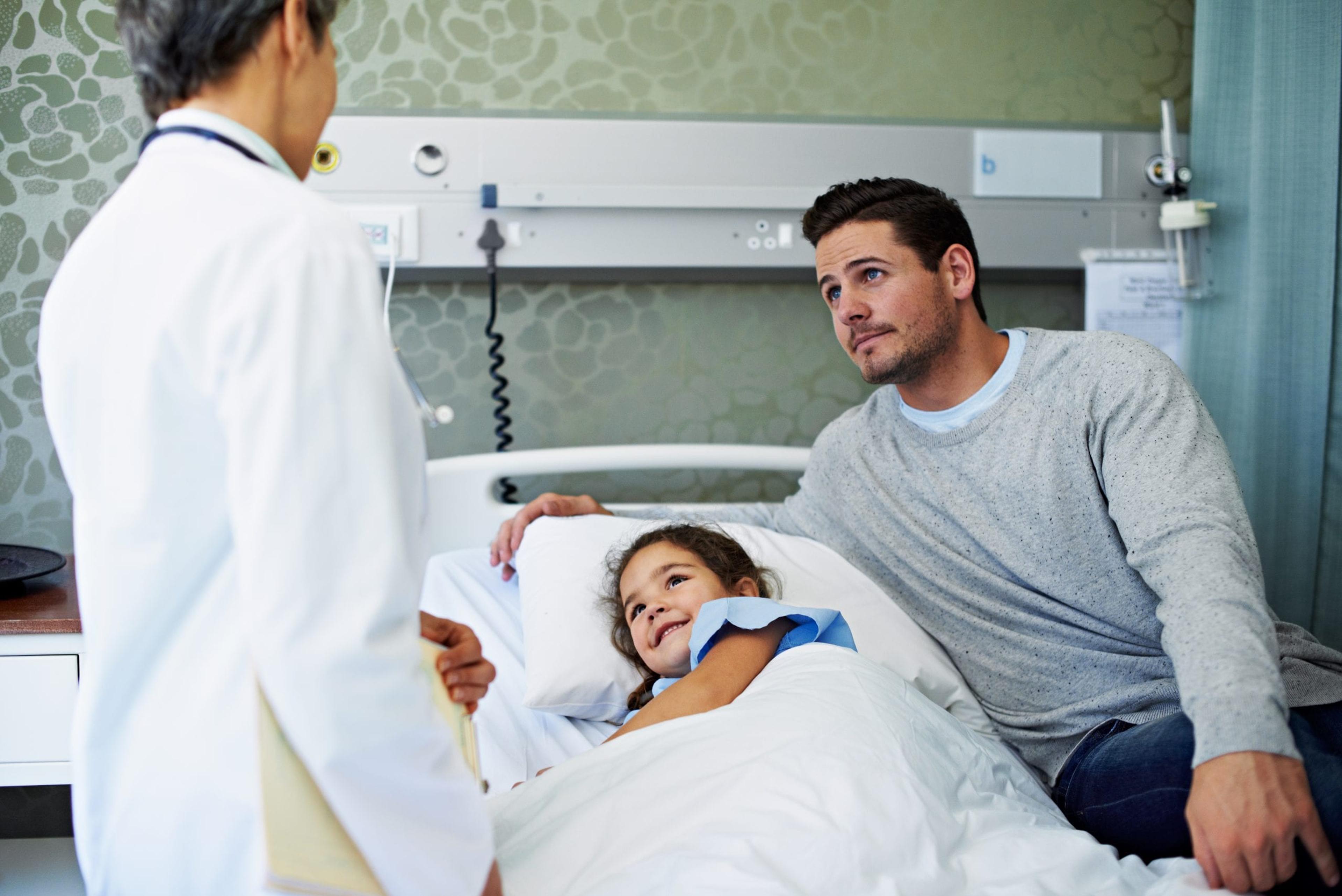 Image of little girl in hospital bed with her dad talking to a doctor.